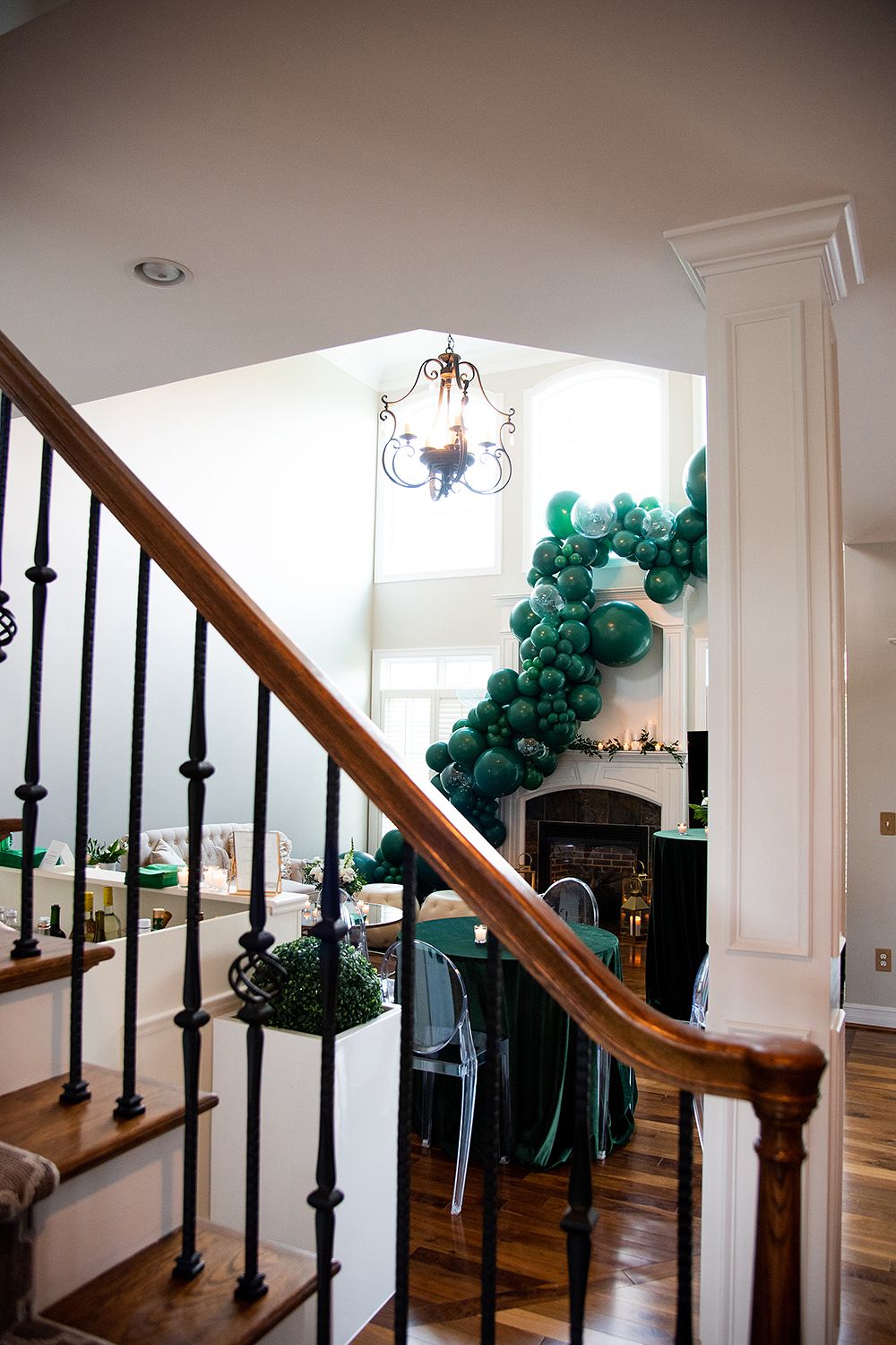 Elegant dark wooden staircase with ornate black iron balusters decorated with green balloon garlands along the handrail.