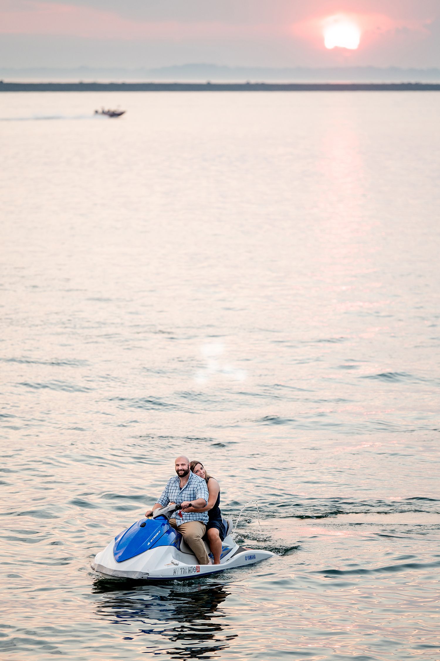 Couple riding a blue jet ski together on calm water at sunset with golden reflections on the surface.