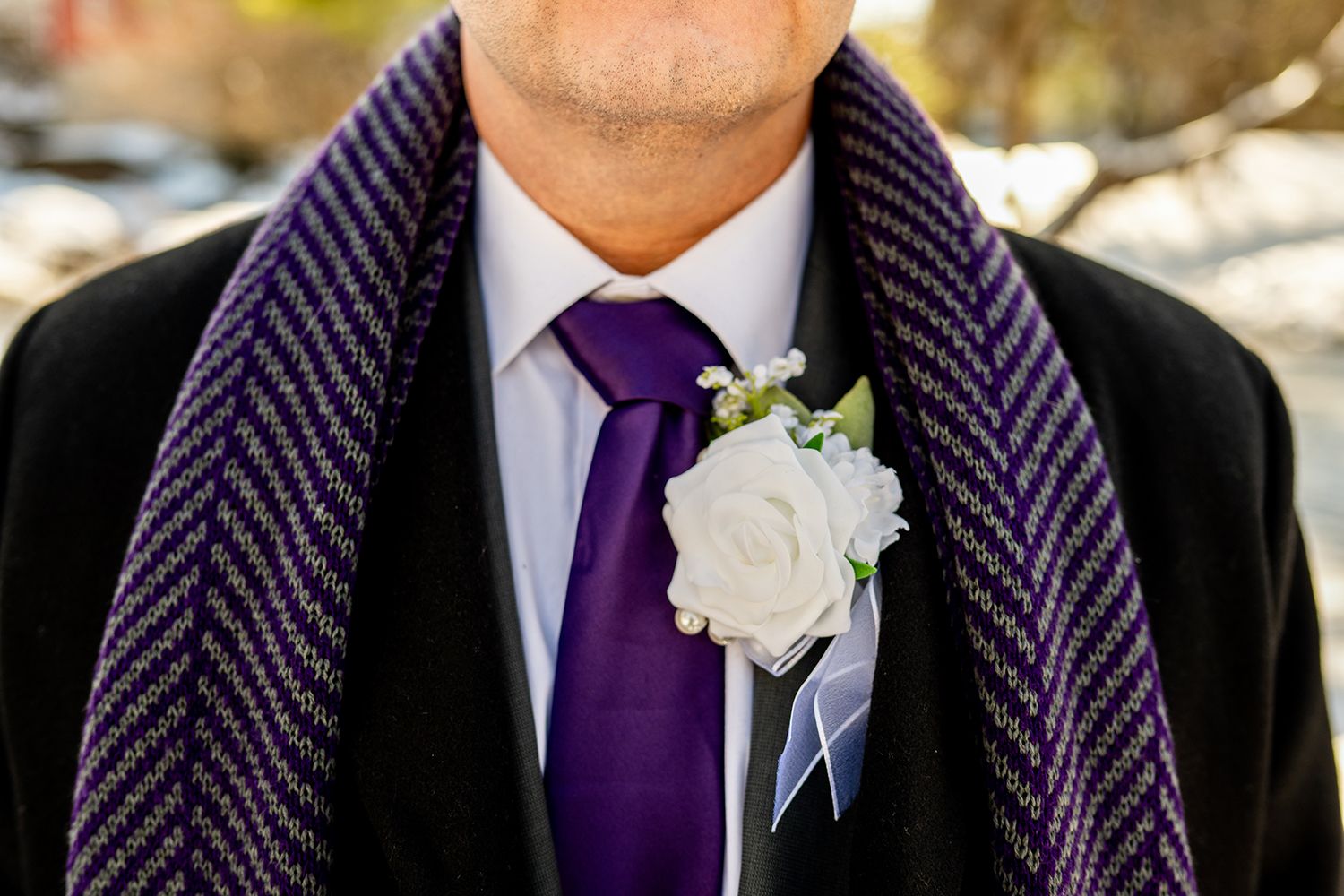 Wedding participants in coordinating black suits and purple ties with white boutonnieres stand in a line.