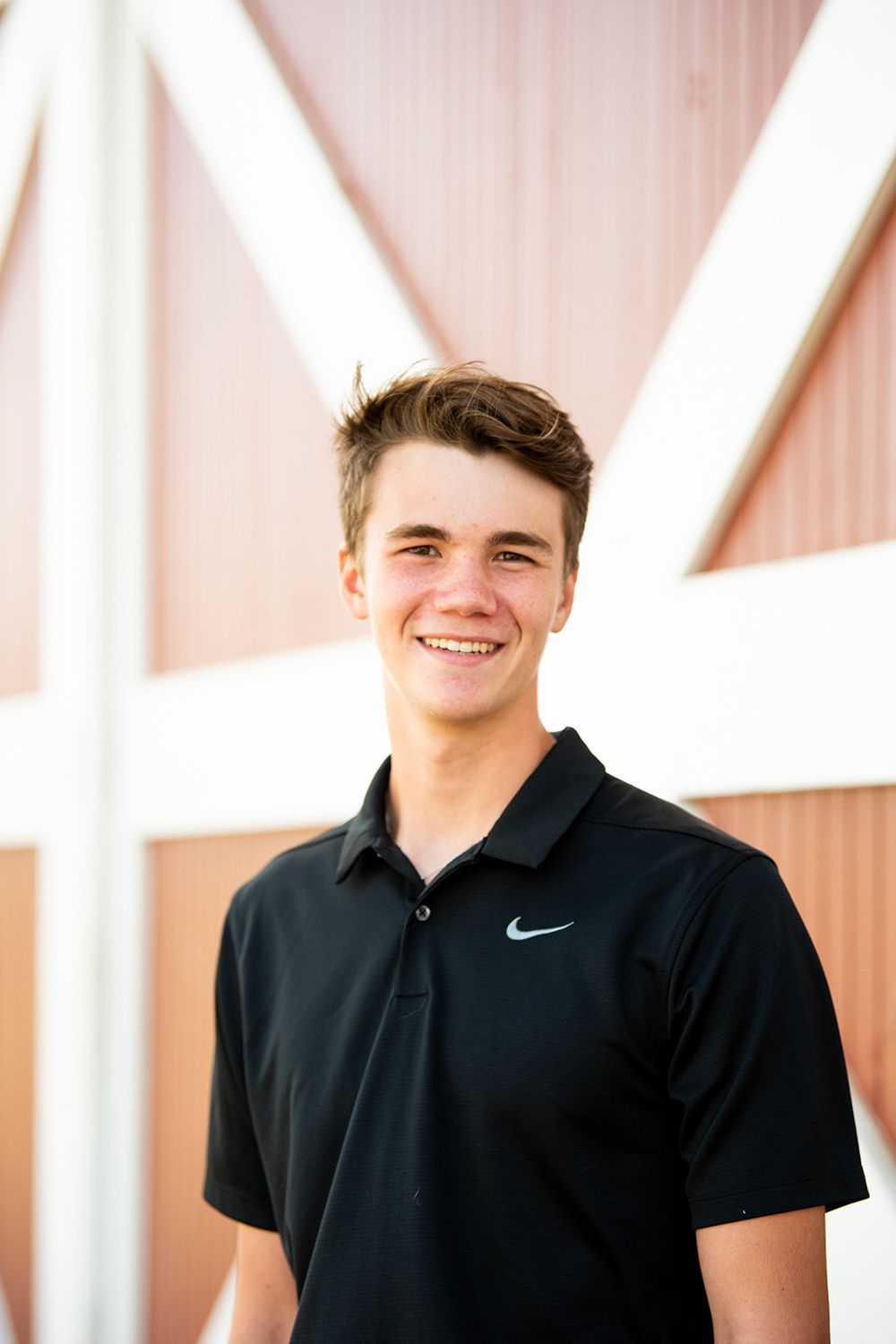 A person wearing a black Nike polo stands smiling in front of a light pink wall with white trim.