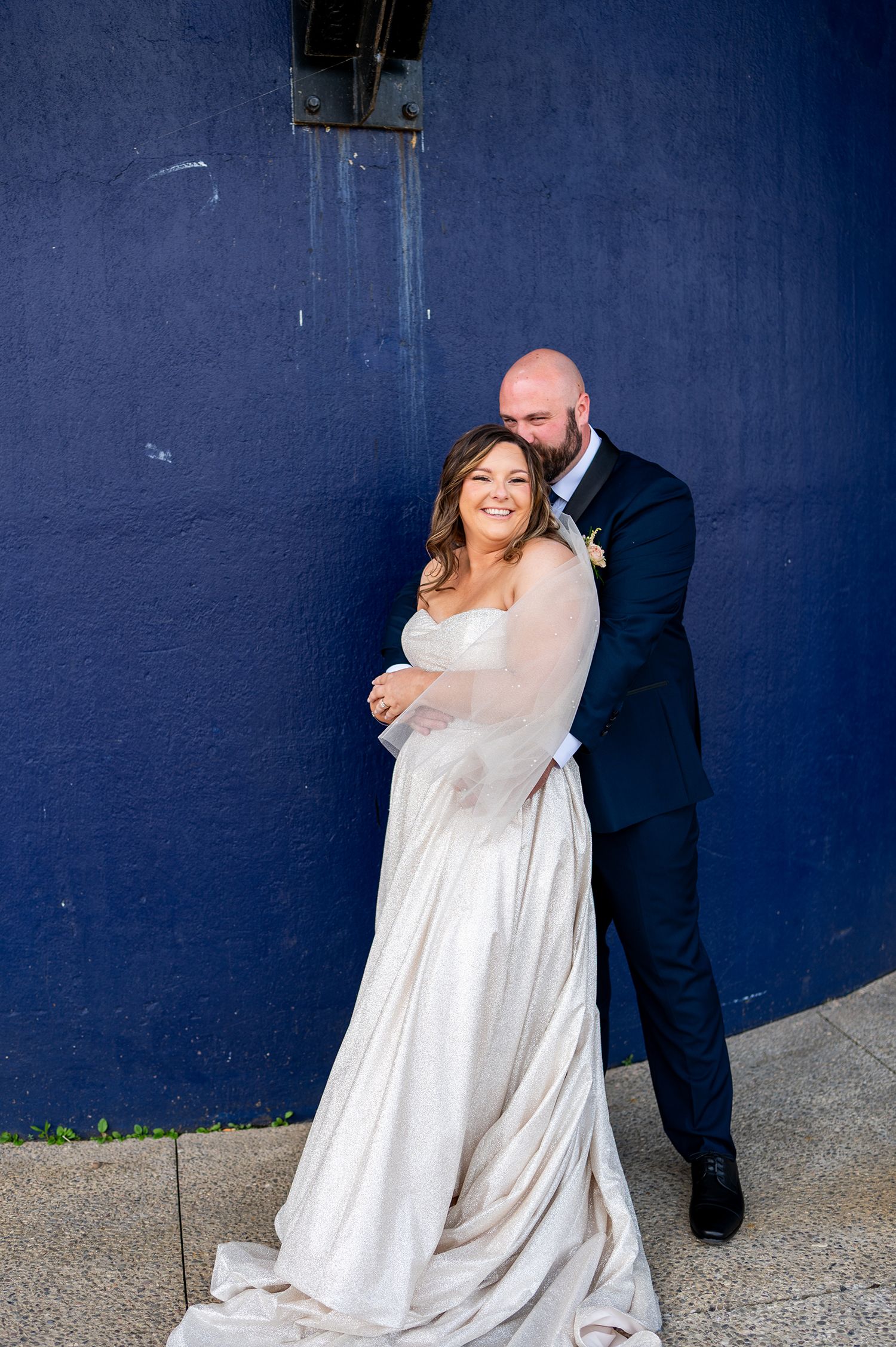 A couple in wedding attire embraces against a deep blue wall in a series of romantic poses.