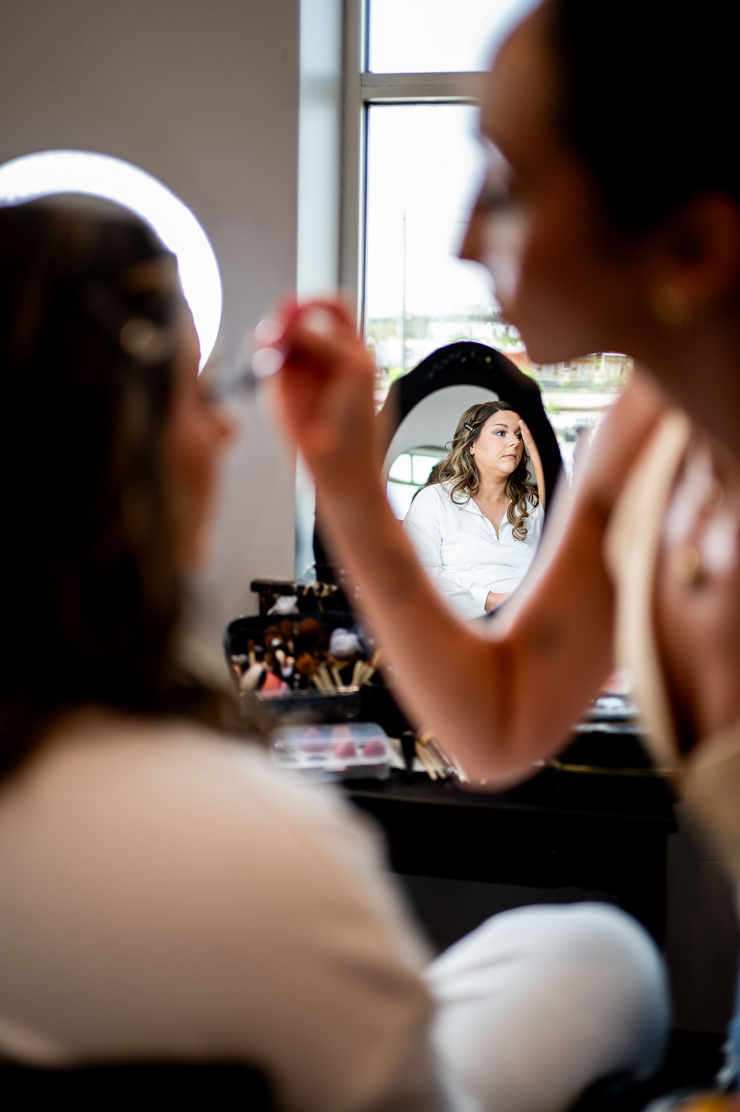 A reflection in a makeup mirror shows someone getting their hair and makeup done during preparation.