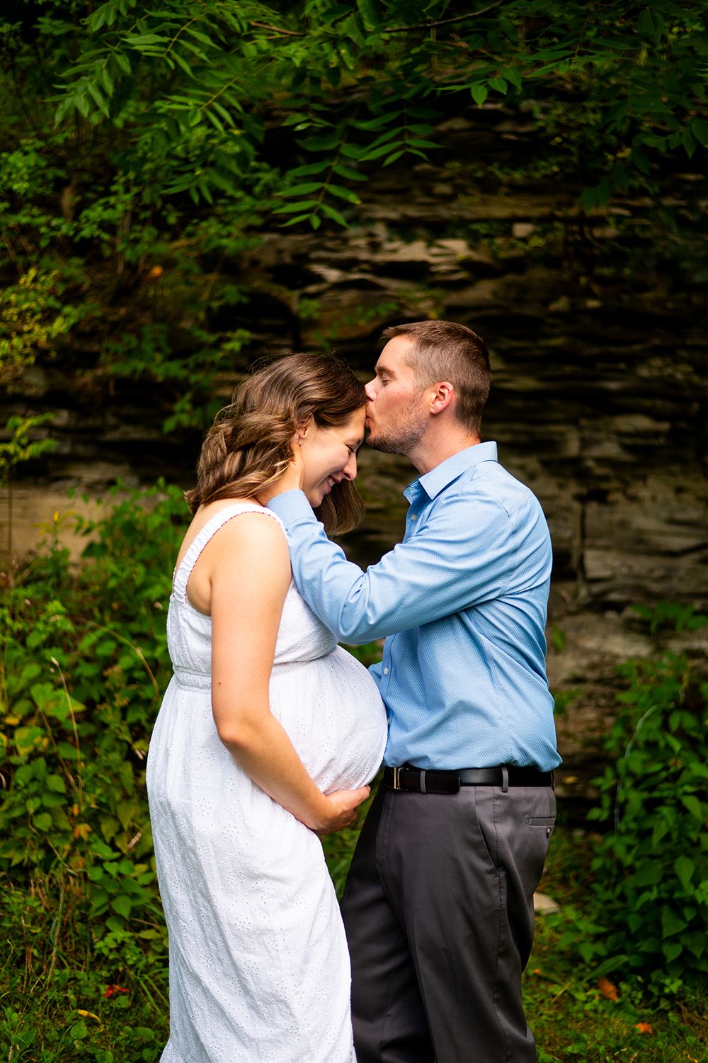 A loving moment shared between a couple in a white dress and blue shirt against a natural stone and greenery backdrop.