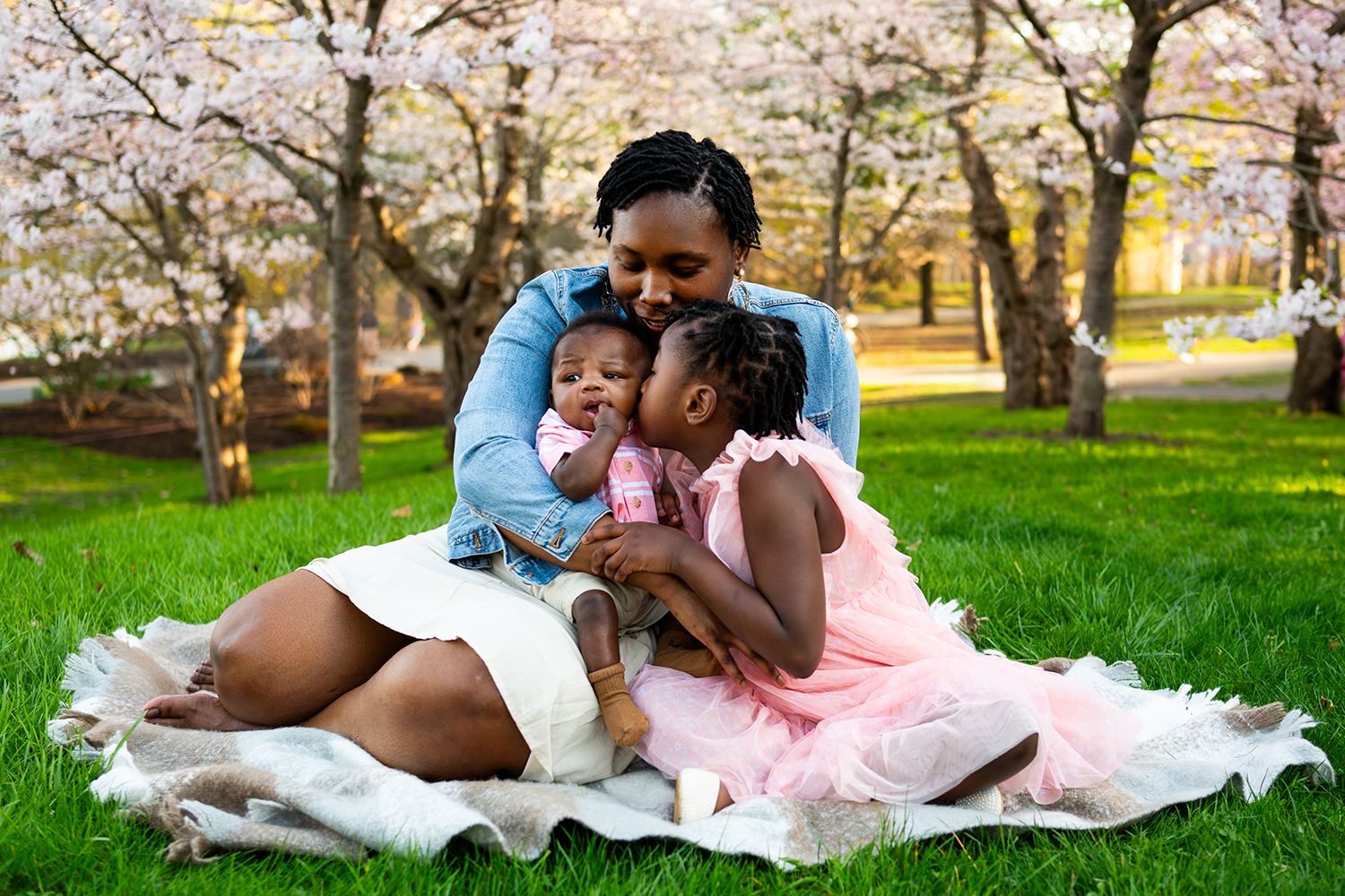 A family shares a joyful moment together on a blanket under blooming cherry blossom trees in a spring park.