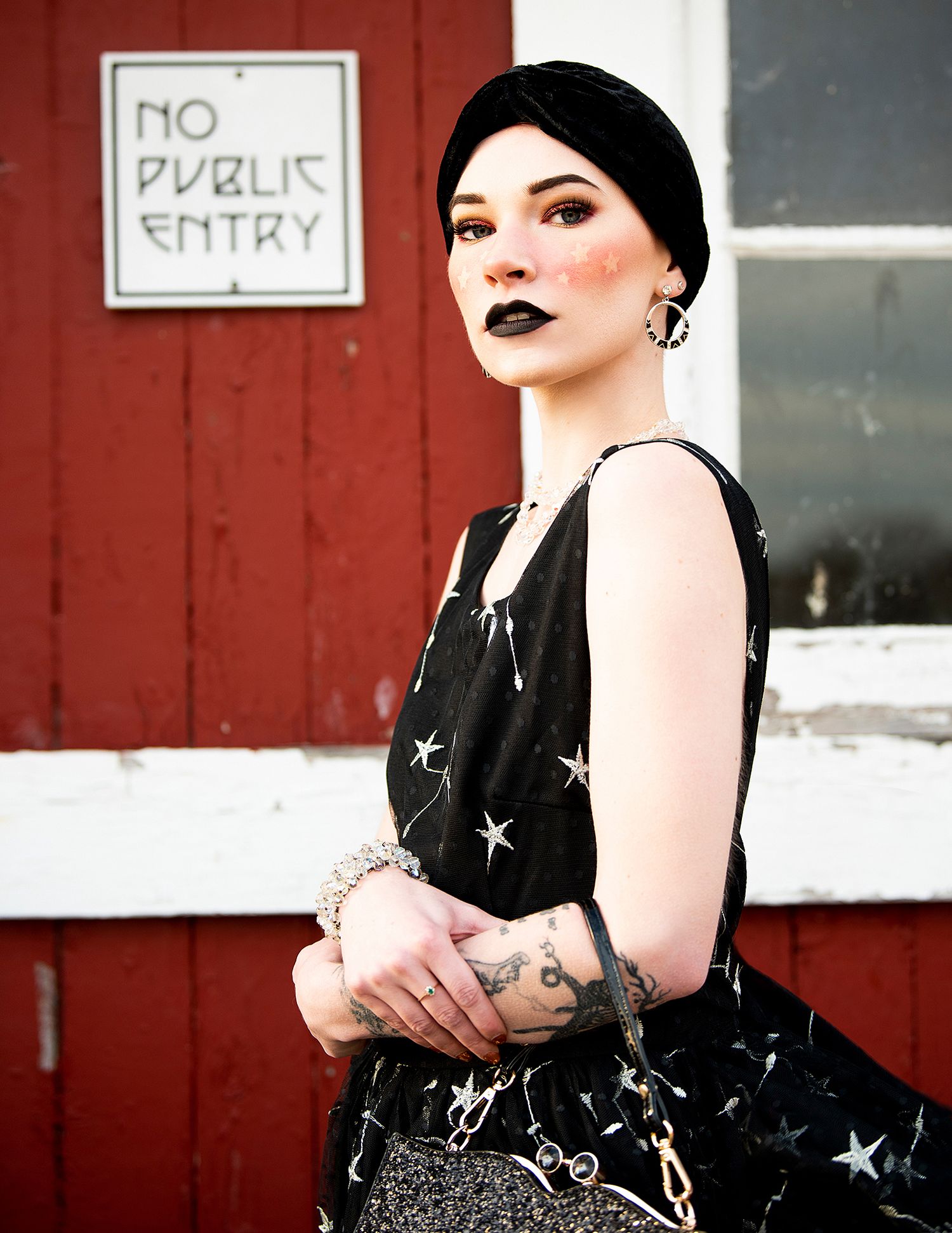 Alternative style fashion against red wall with 'No Public Entry' sign featuring dark dress with star pattern.