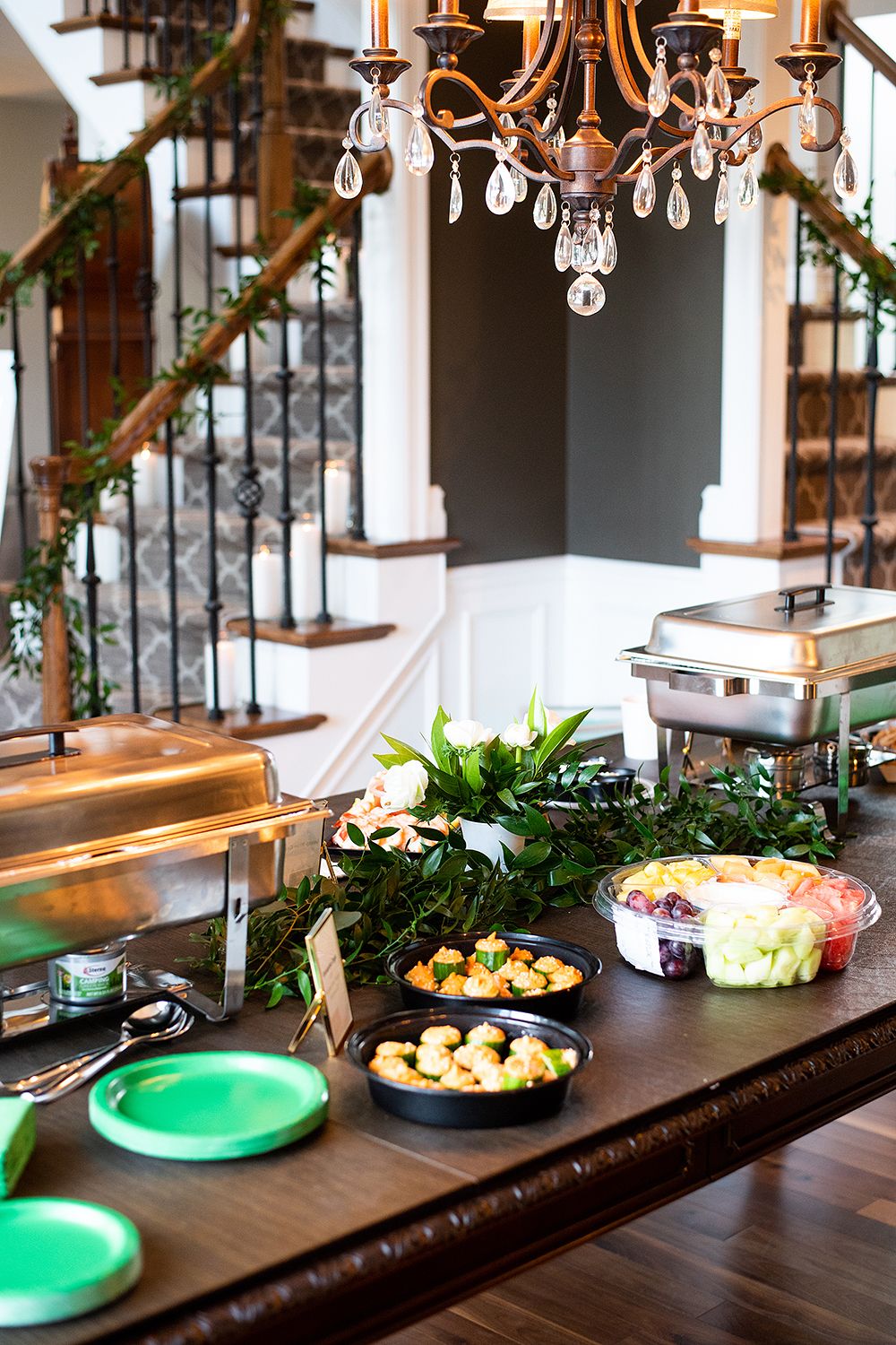 Elegant buffet setup with chafing dishes and appetizers under a crystal chandelier in an upscale dining space.