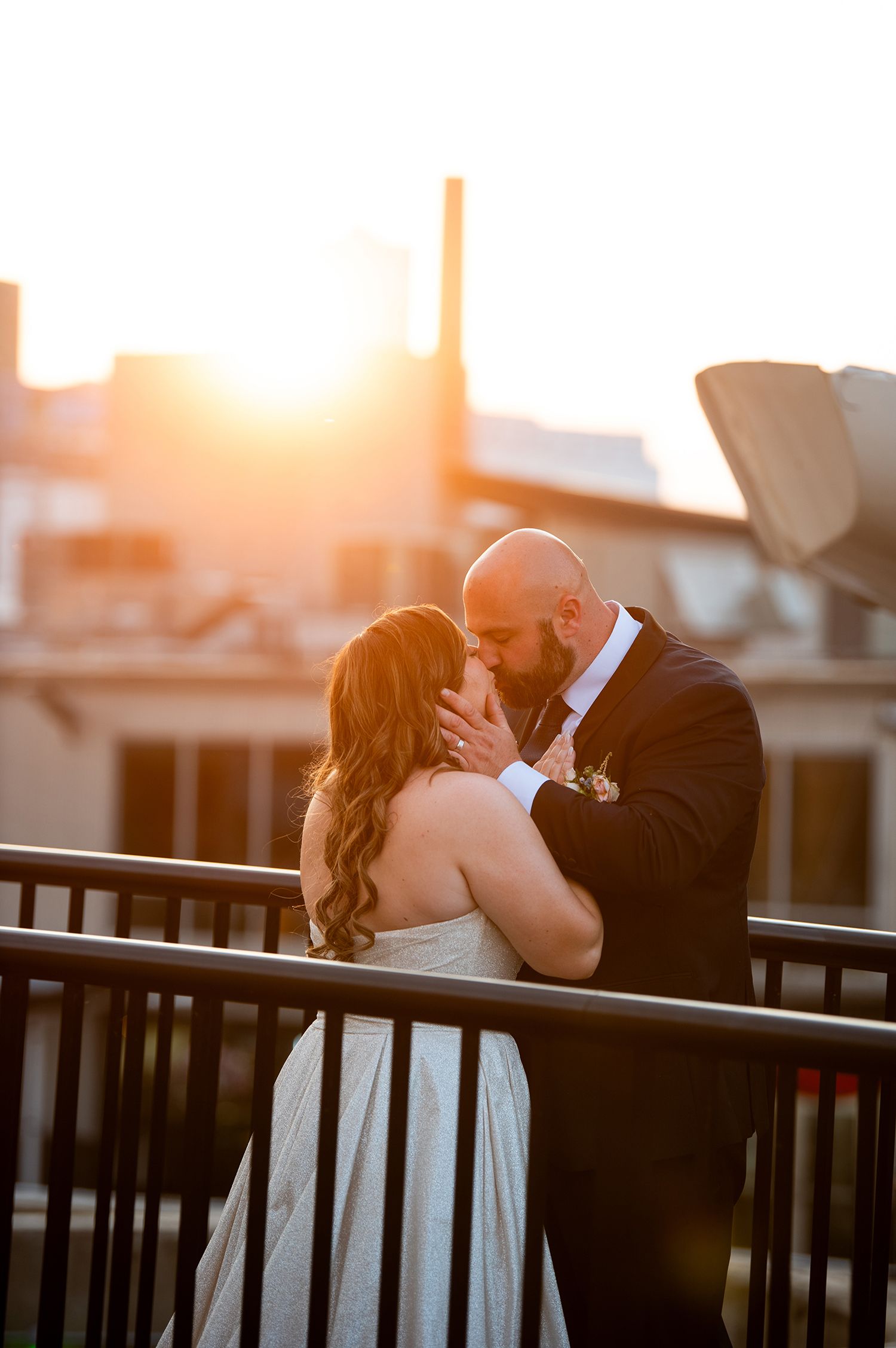 Romantic sunset silhouette sequence of newlyweds kissing against black railings at golden hour.