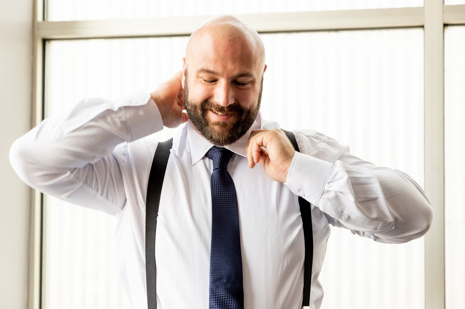 Professional in a navy suit and tie speaks on a mobile phone while standing near bright windows in an office setting.