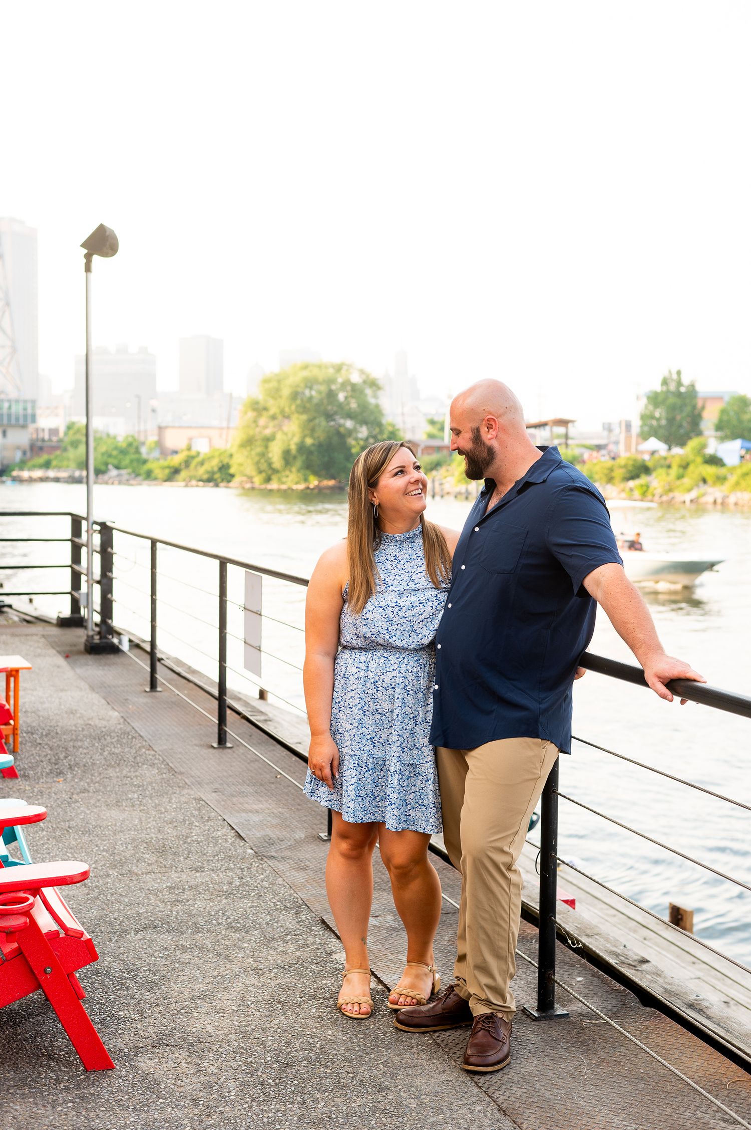 Happy couple standing close on a riverside promenade with city skyline in the background.