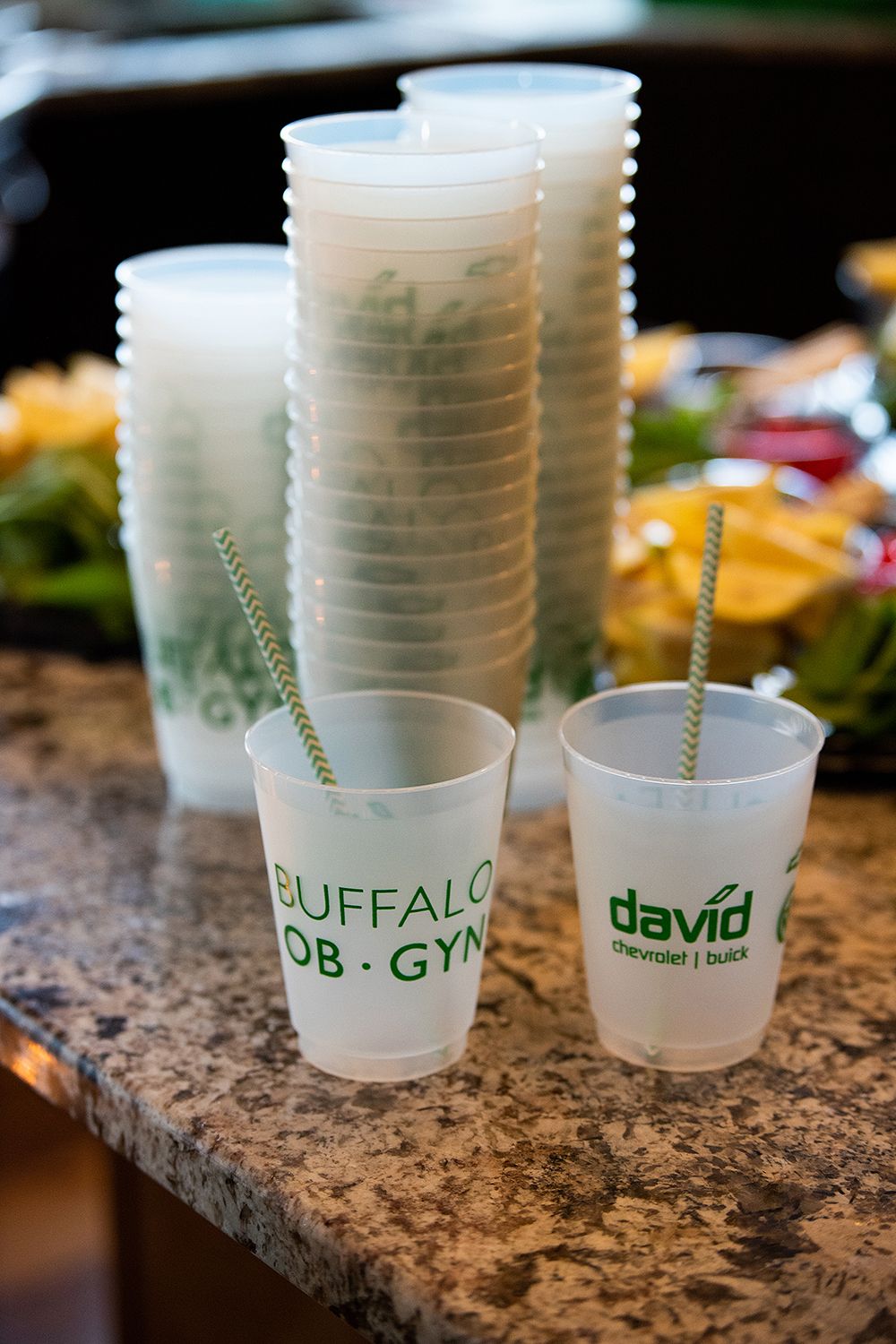 Branded plastic cups with straws stacked on a granite countertop showing Buffalo OB GYN and David logos.