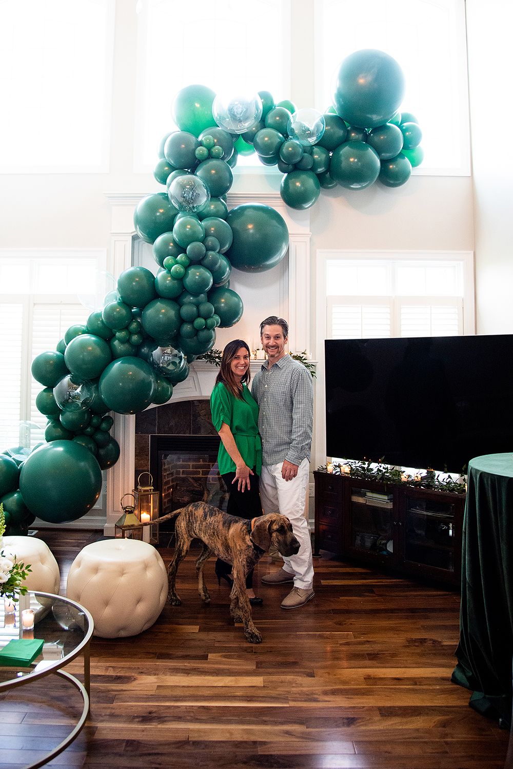 Green balloon arch installation creates an elegant backdrop in a modern room with hardwood floors and natural light.