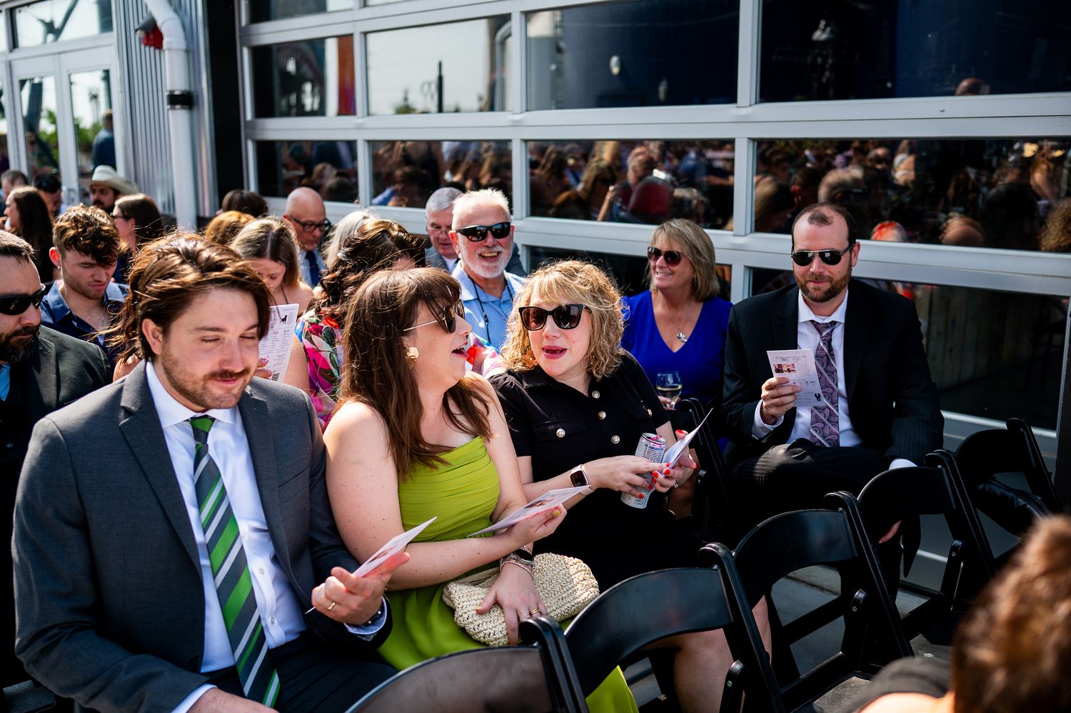 Wedding guests seated in rows of black chairs during an outdoor ceremony.