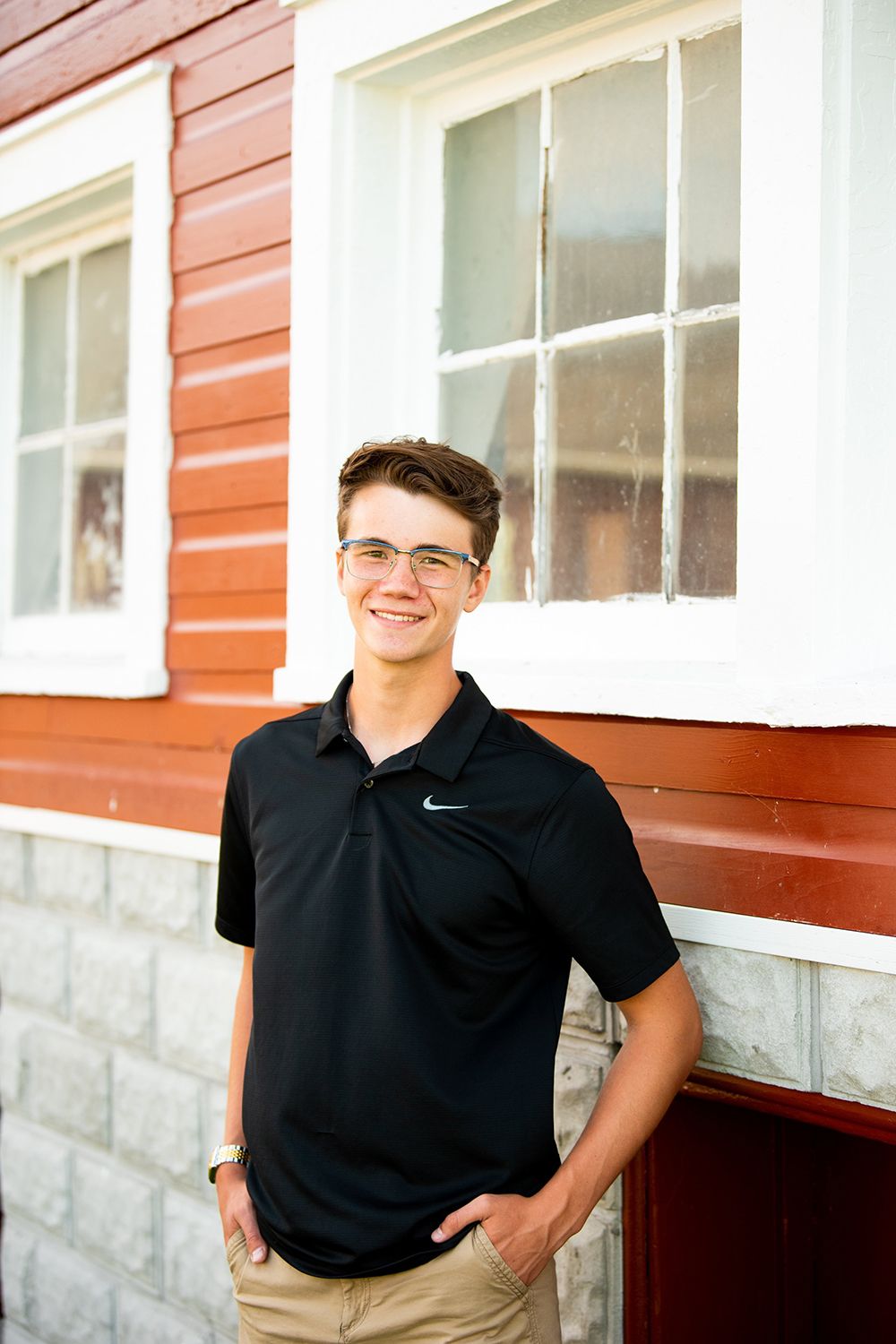 A casual portrait against a red building exterior with white trim windows and stone foundation.
