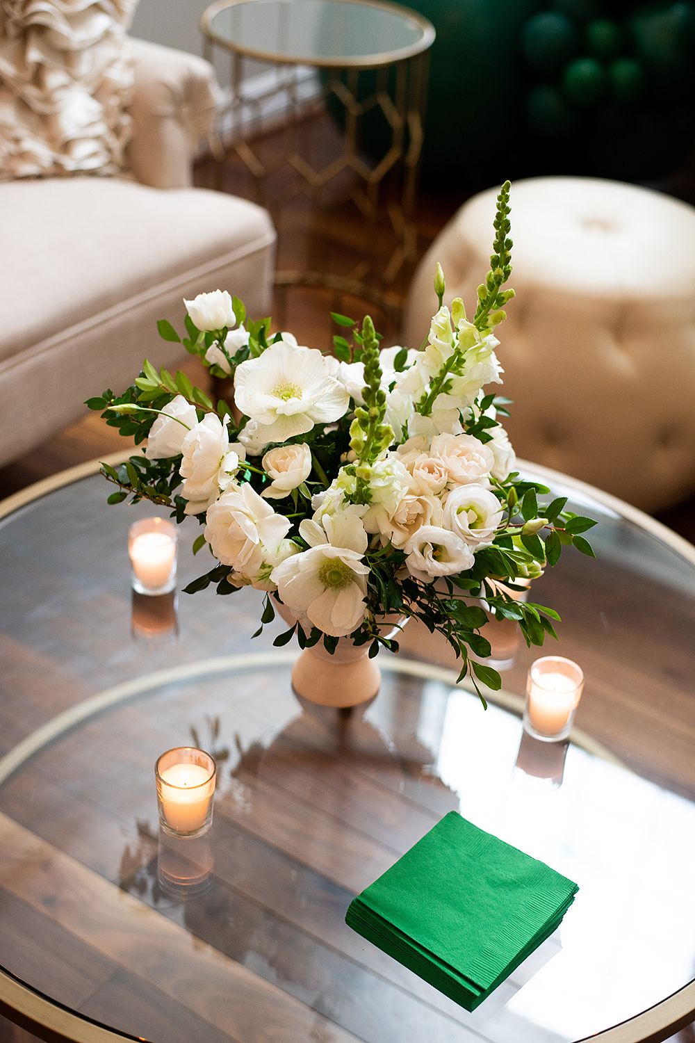 Elegant floral centerpiece with white and blush roses on mirrored coffee table with candlelight and emerald green napkins.