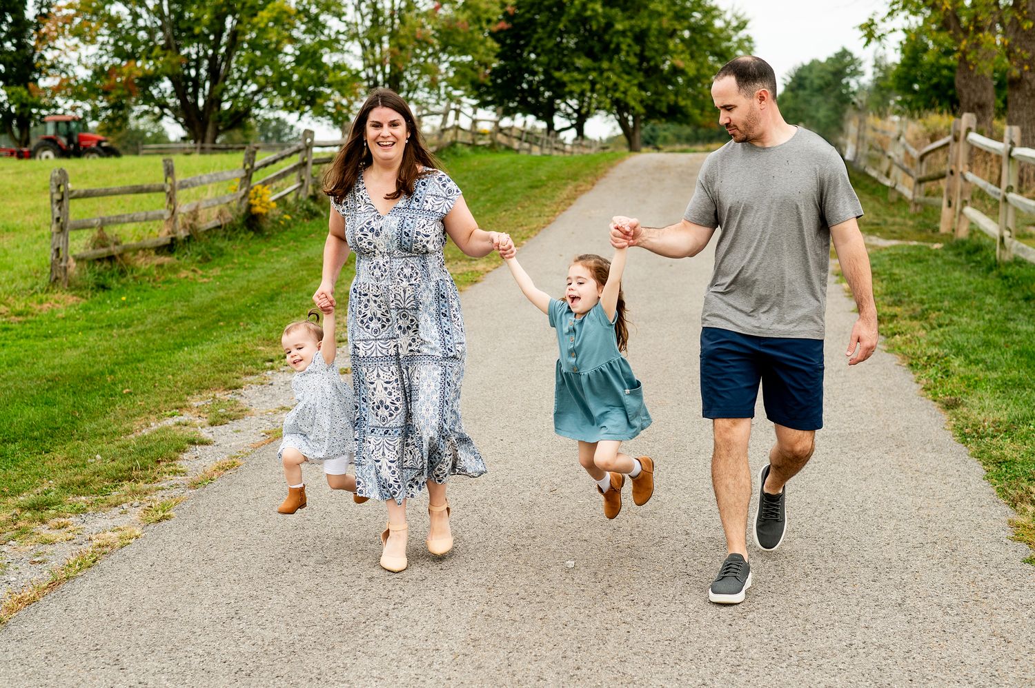 Happy family of four walking hand-in-hand on a scenic path, parents swinging two young daughters outdoors.