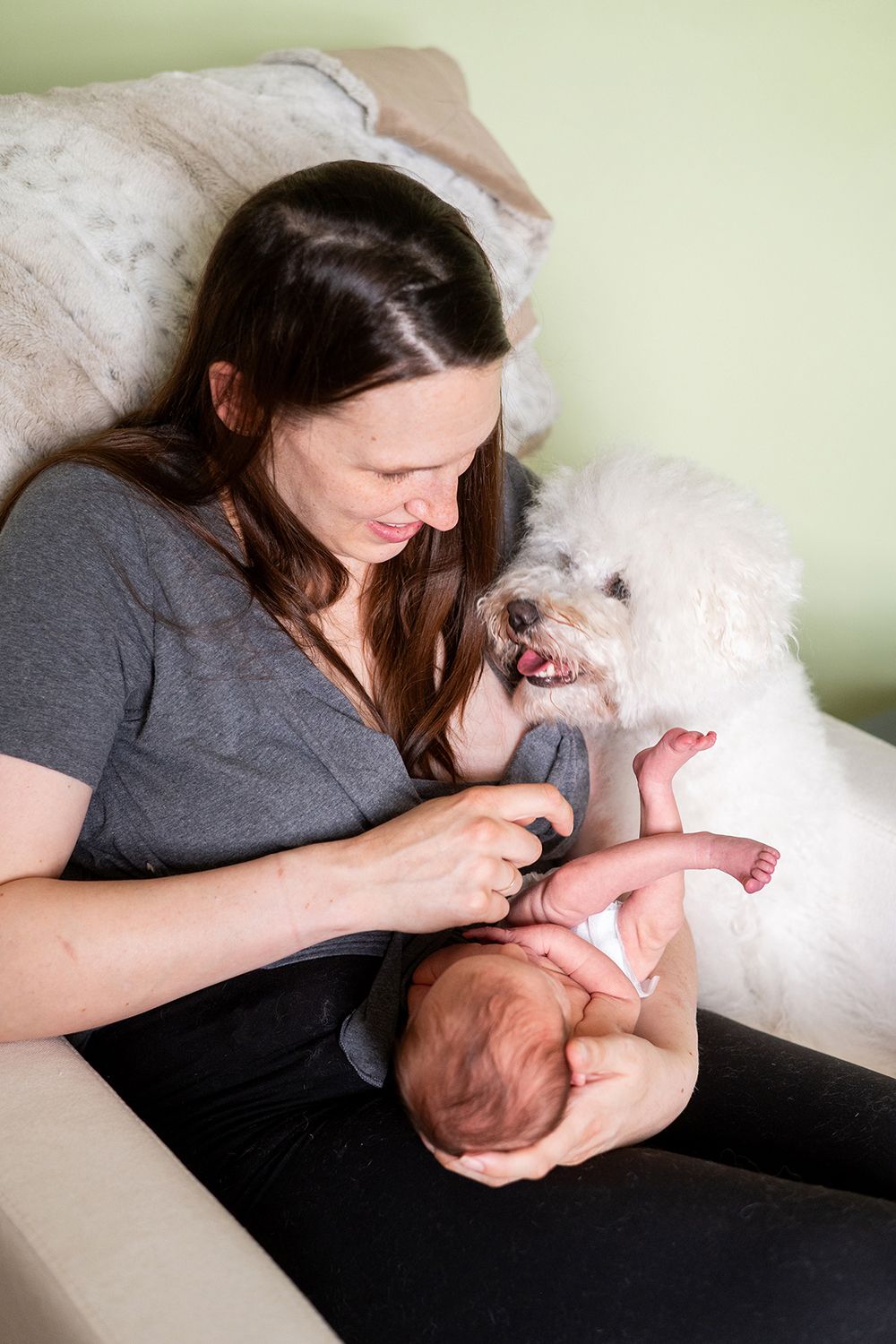 A tender moment between a mother, baby and white dog on a couch at home.