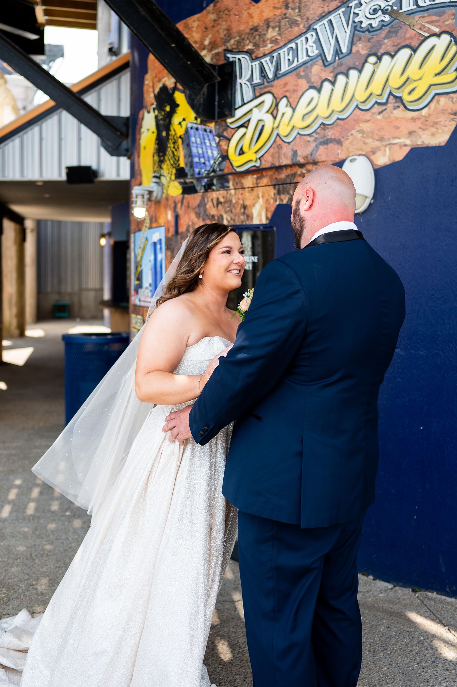 A couple shares a romantic moment outside a rustic brick building with signage during their wedding celebration.