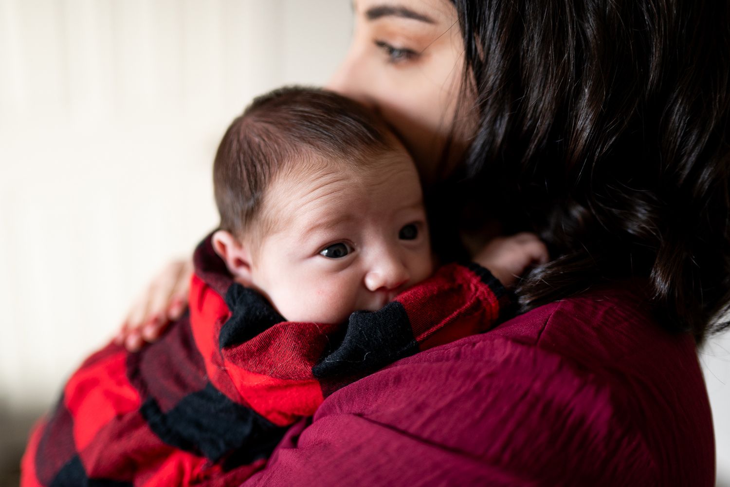 Peaceful newborn resting on cozy white fur wearing festive red buffalo check clothing.
