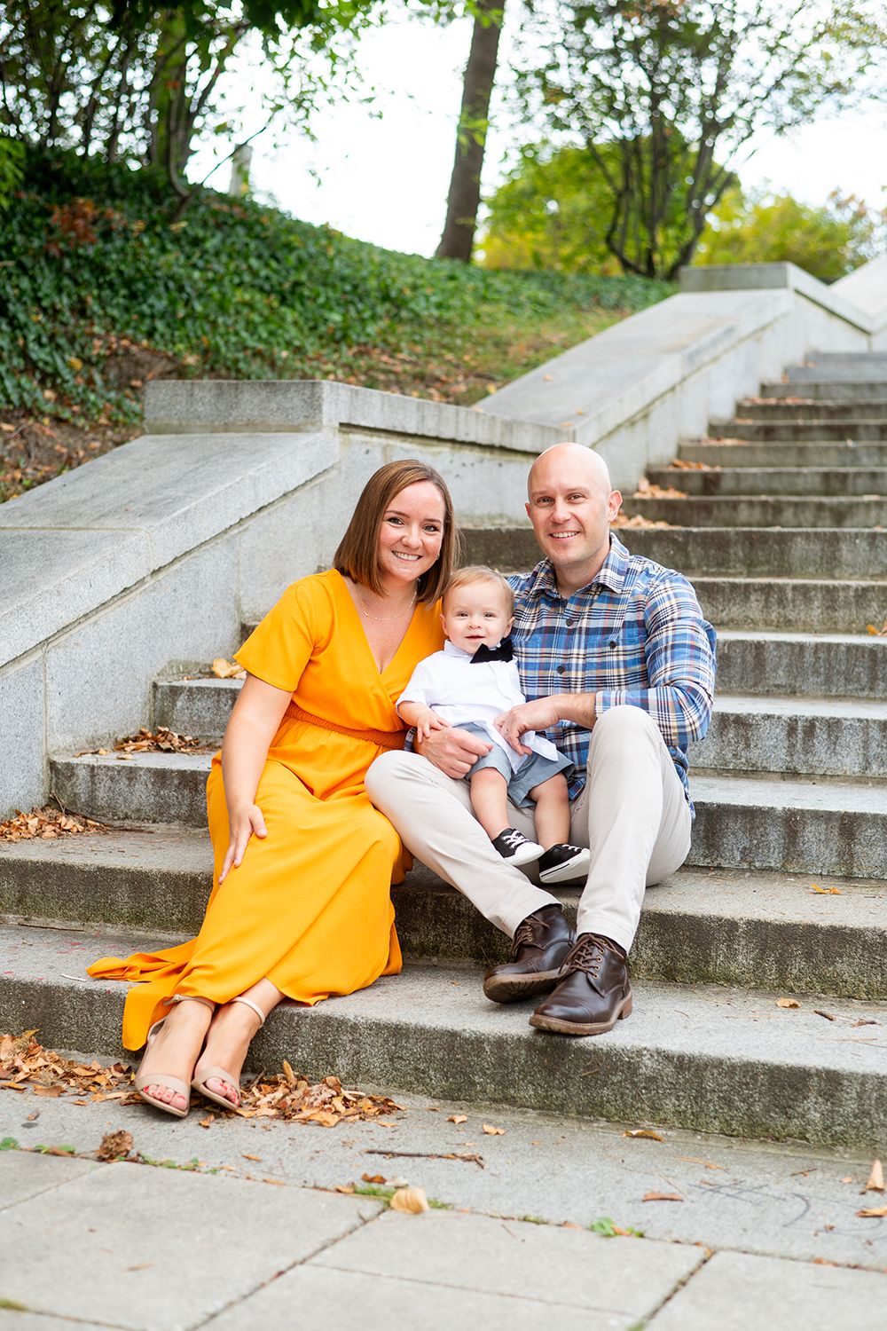 A family sits together on outdoor concrete steps during fall, with trees and ivy in the background.