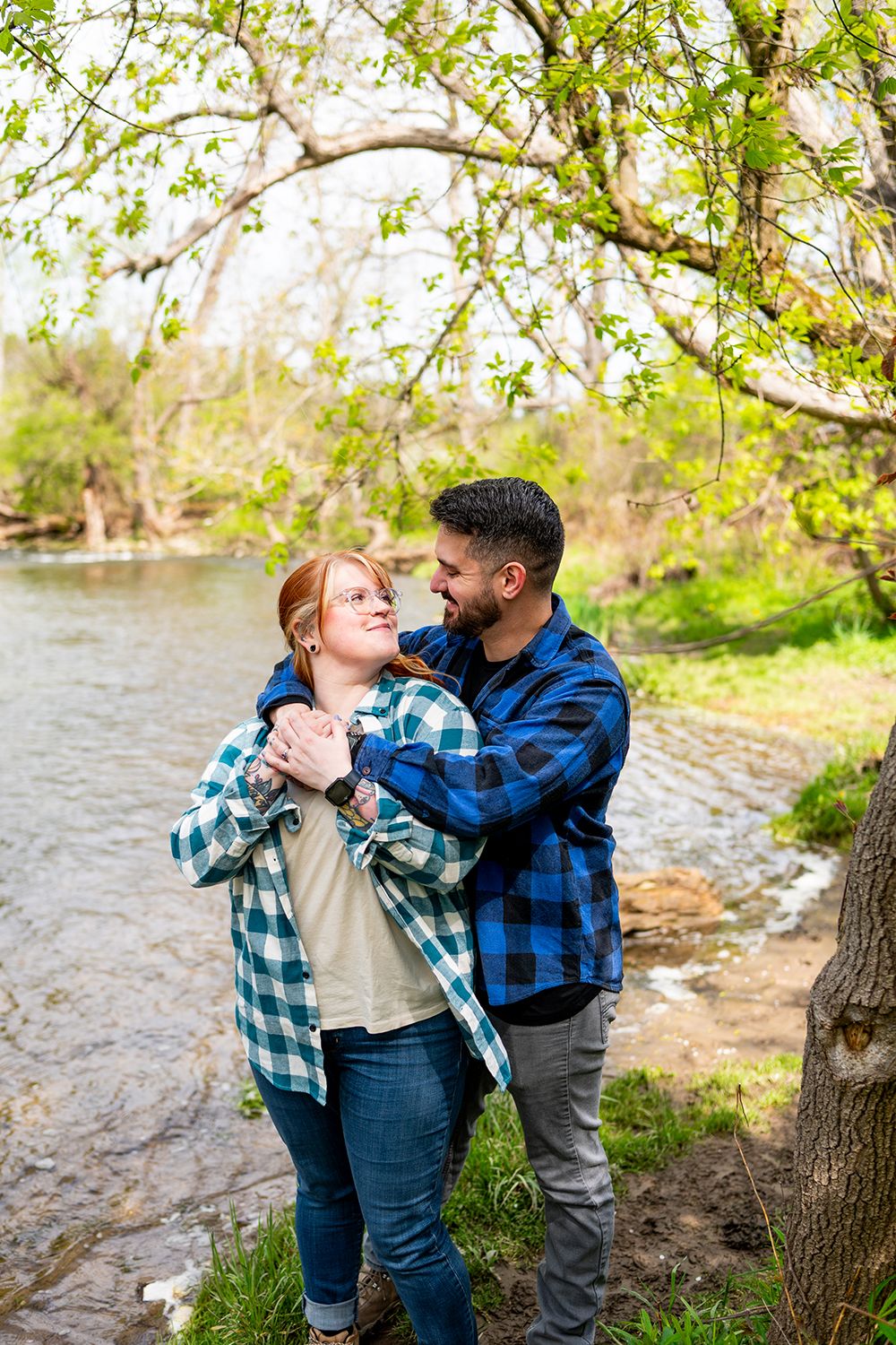 Couple in coordinating plaid and denim outfits share tender moments by a river in springtime.