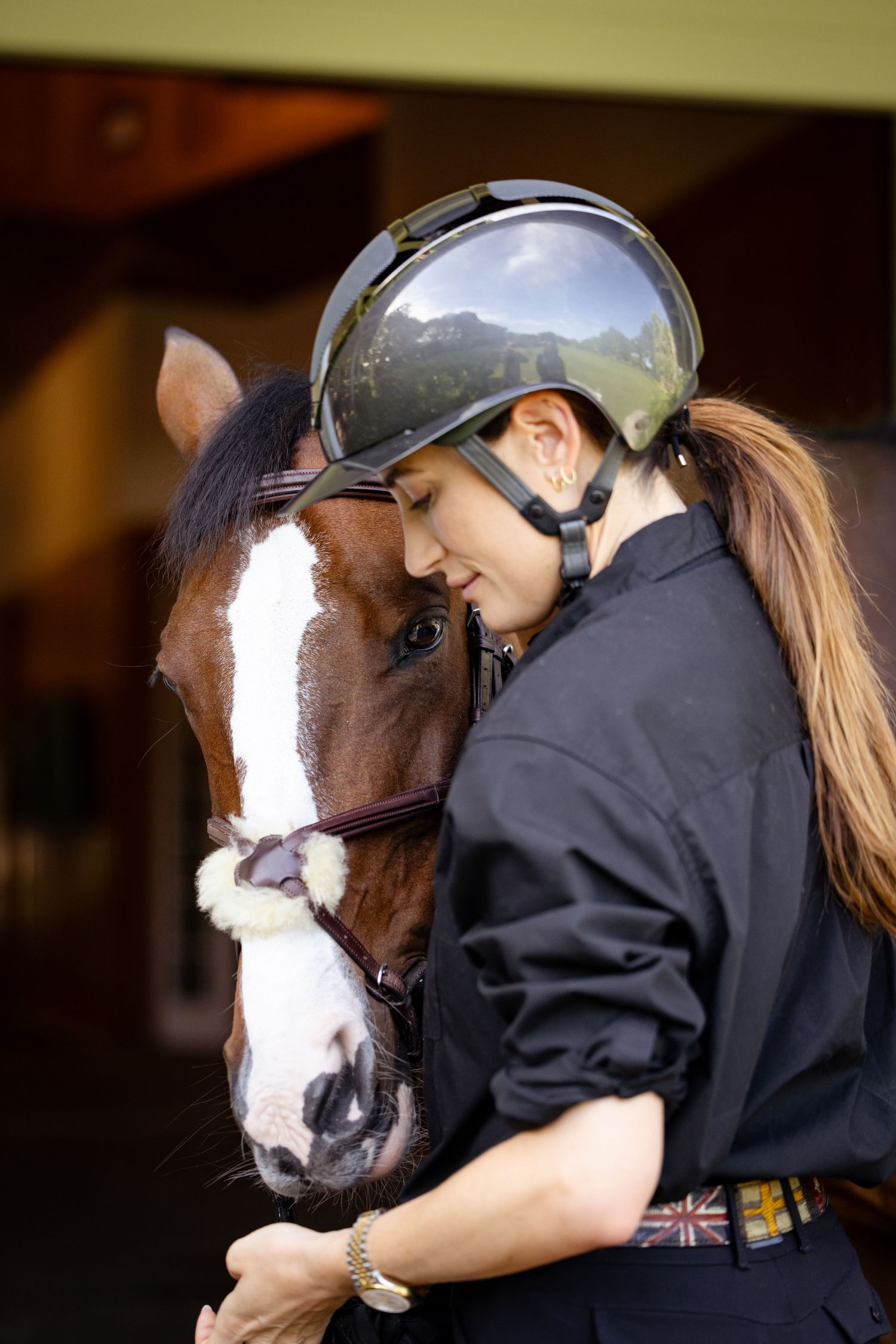 Close-up shot of rider in helmet sharing tender moment with brown and white horse.