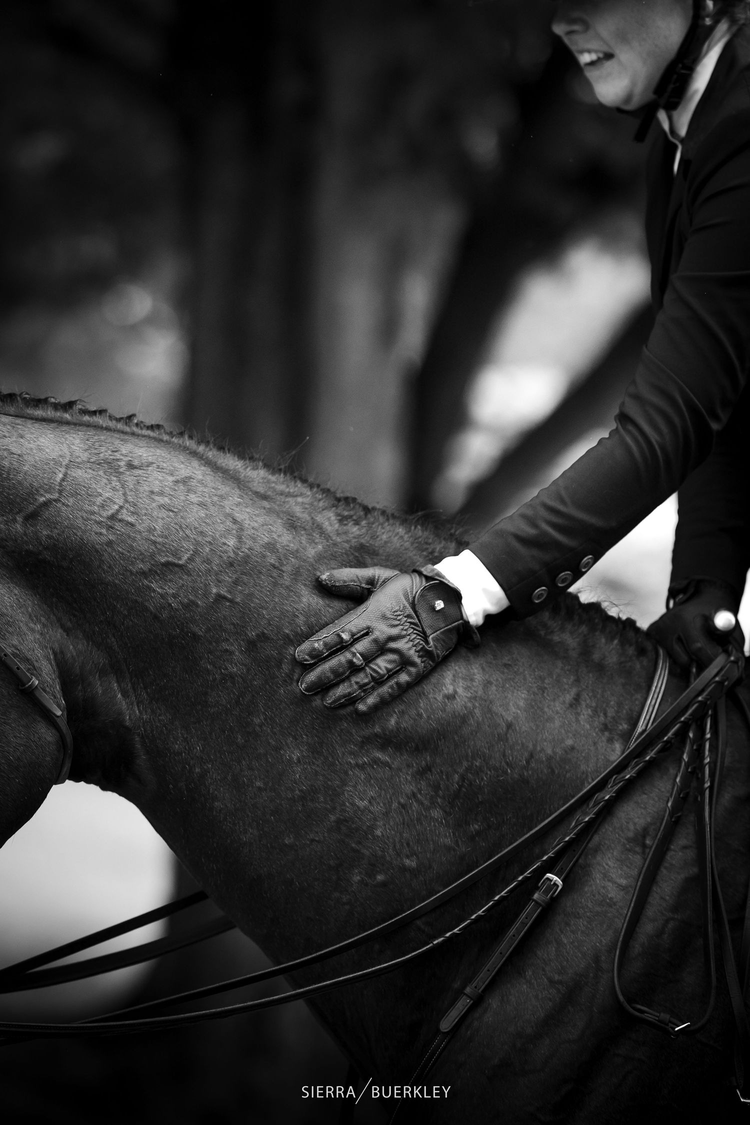 Professional equestrian in formal attire patting black horse in dramatic black and white photograph.