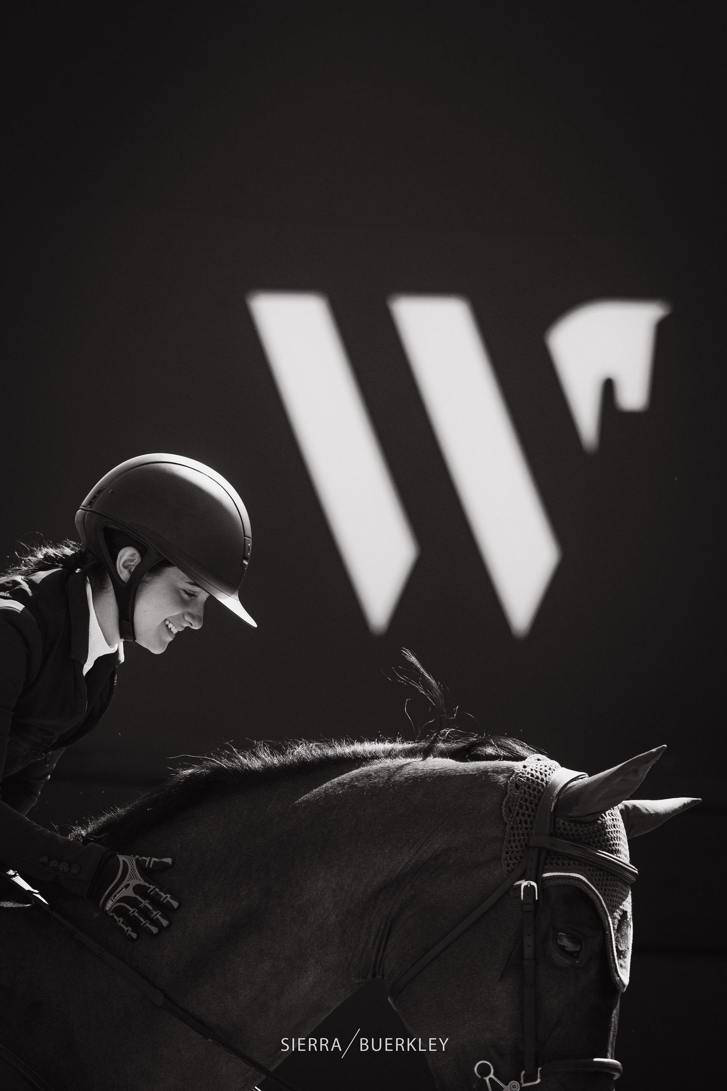 Artistic black and white equestrian photo with dramatic lighting and W logo in background.
