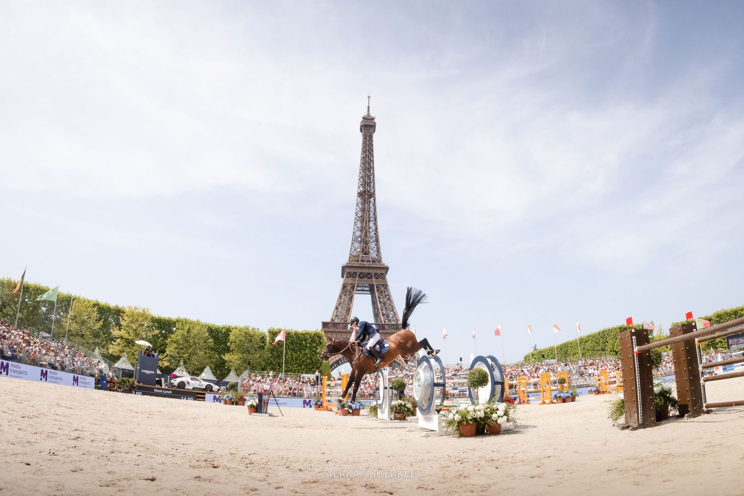 The iconic Eiffel Tower stands tall in Paris with crowds enjoying the grassy Champ de Mars on a sunny day.