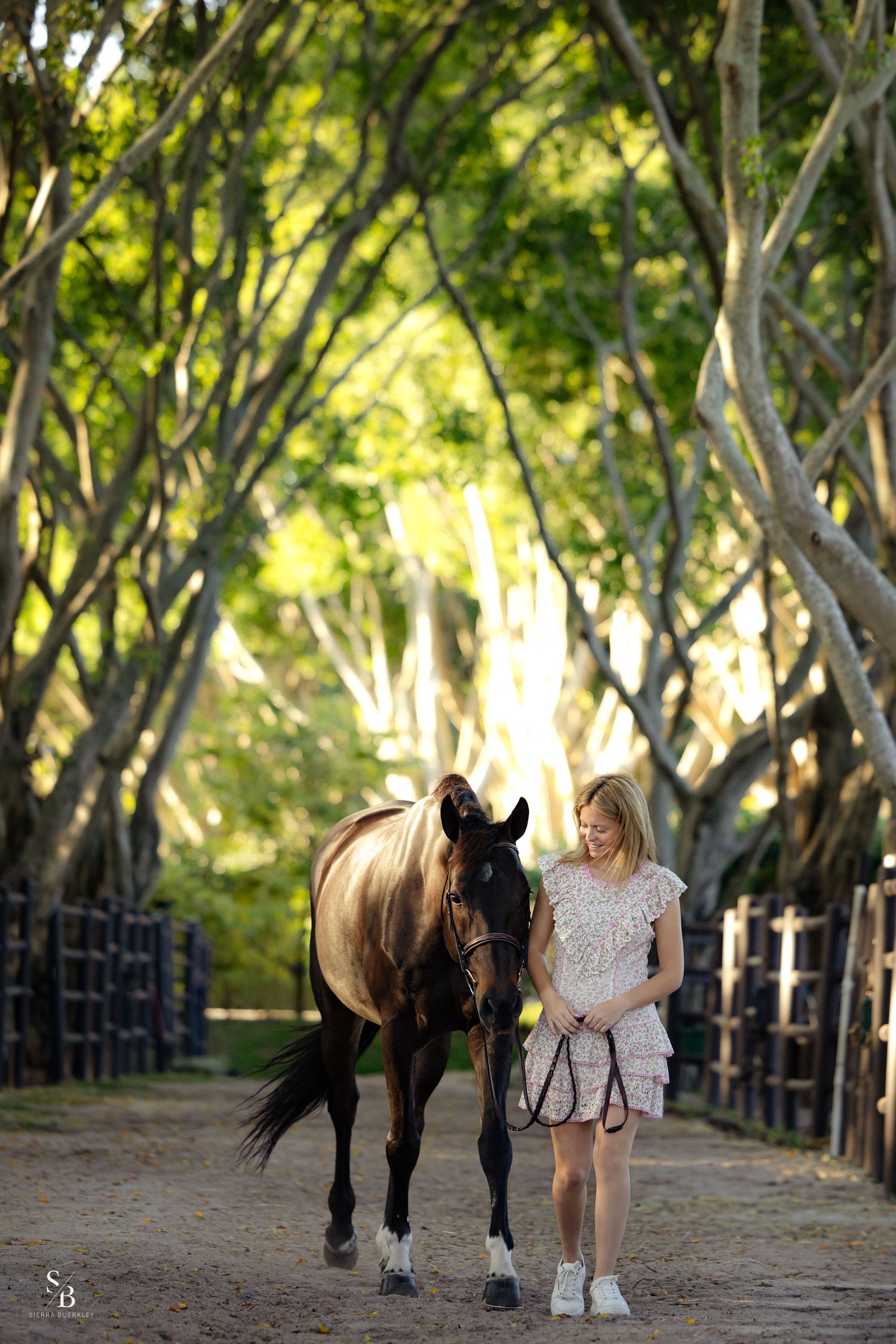 A young equestrian walks alongside their horse down a tree-lined path.