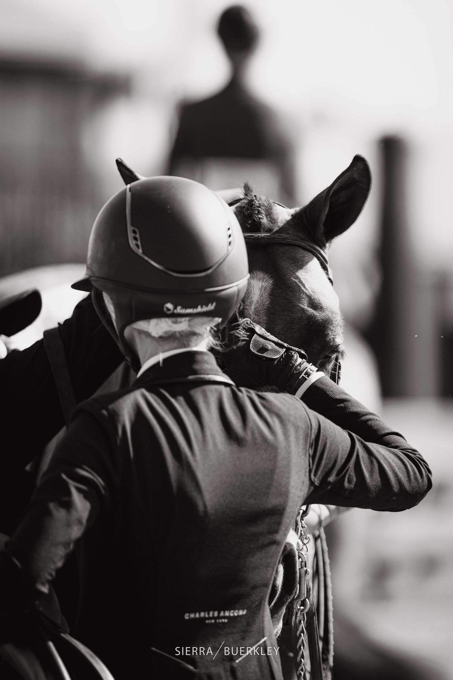 Black and white close-up of a rider wearing a helmet embracing their horse.