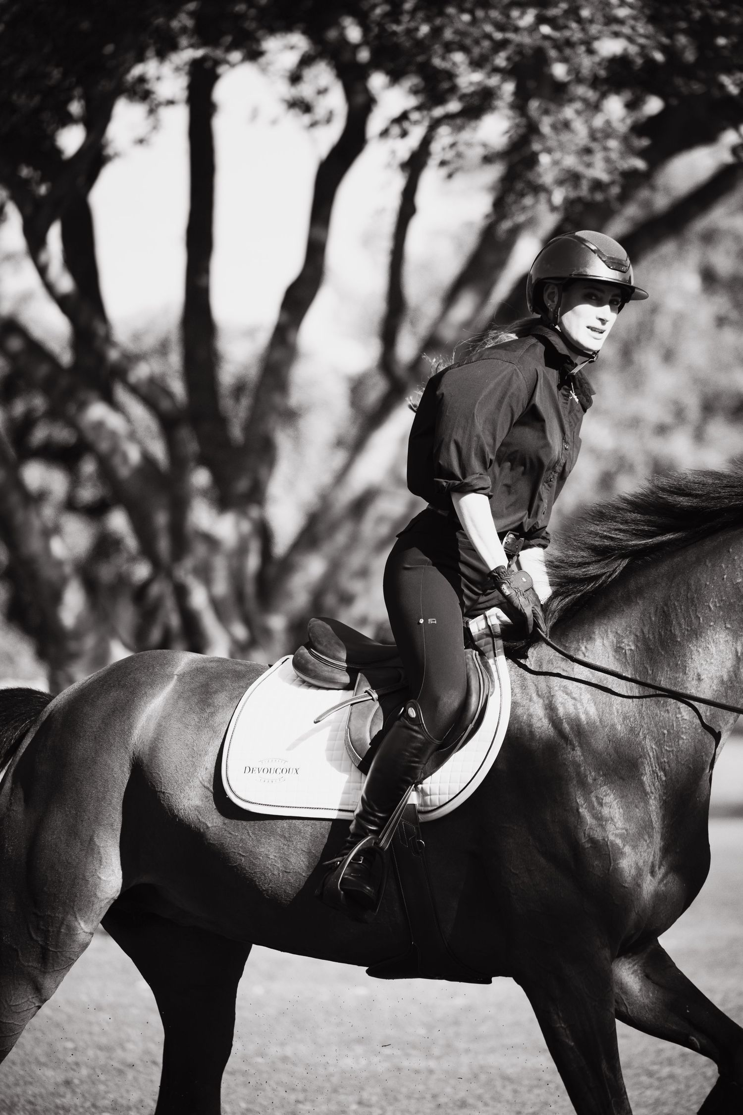 Black and white photo of an equestrian rider on a dark horse in a wooded setting.
