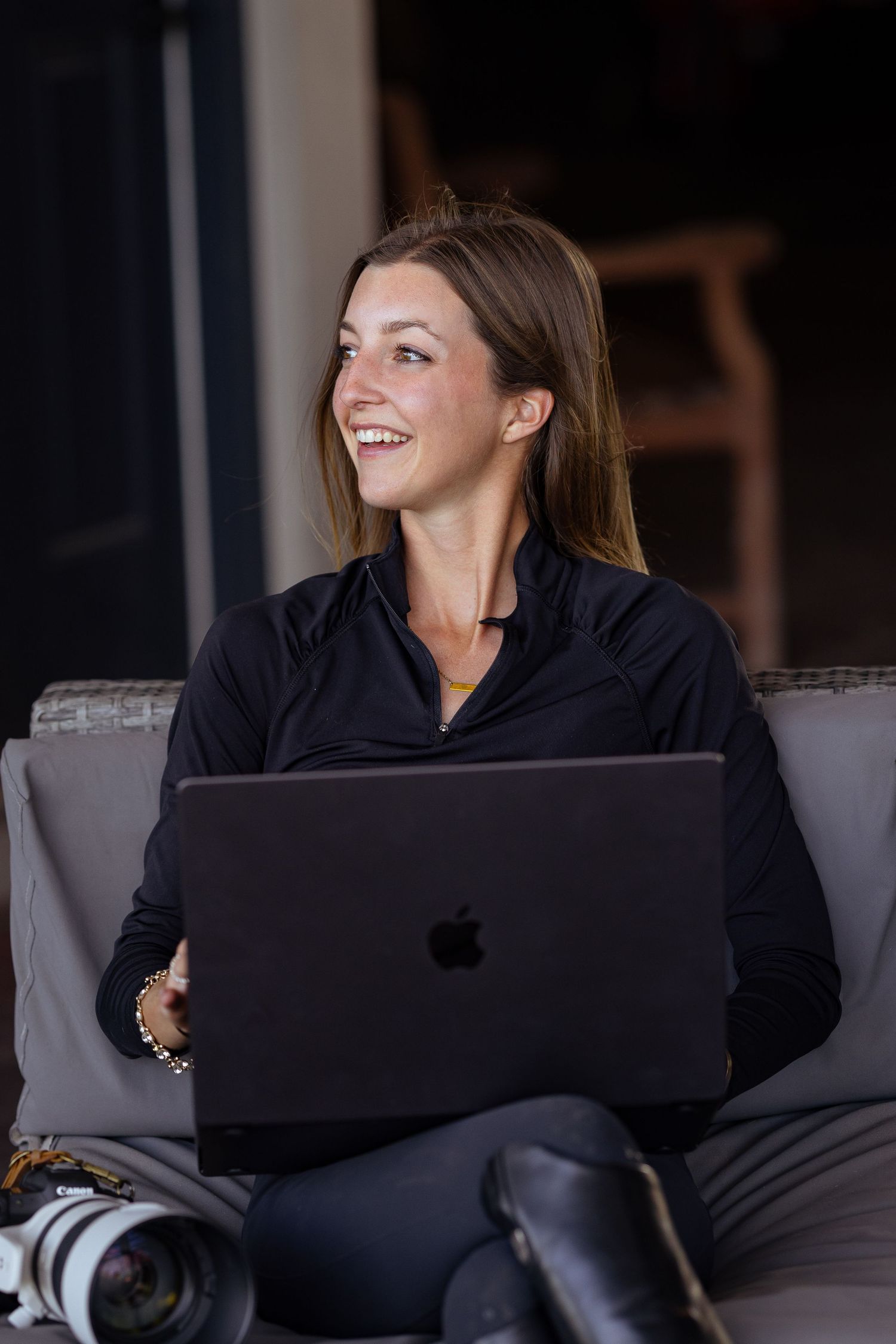 Woman in navy shirt works on laptop with equestrian gear nearby.