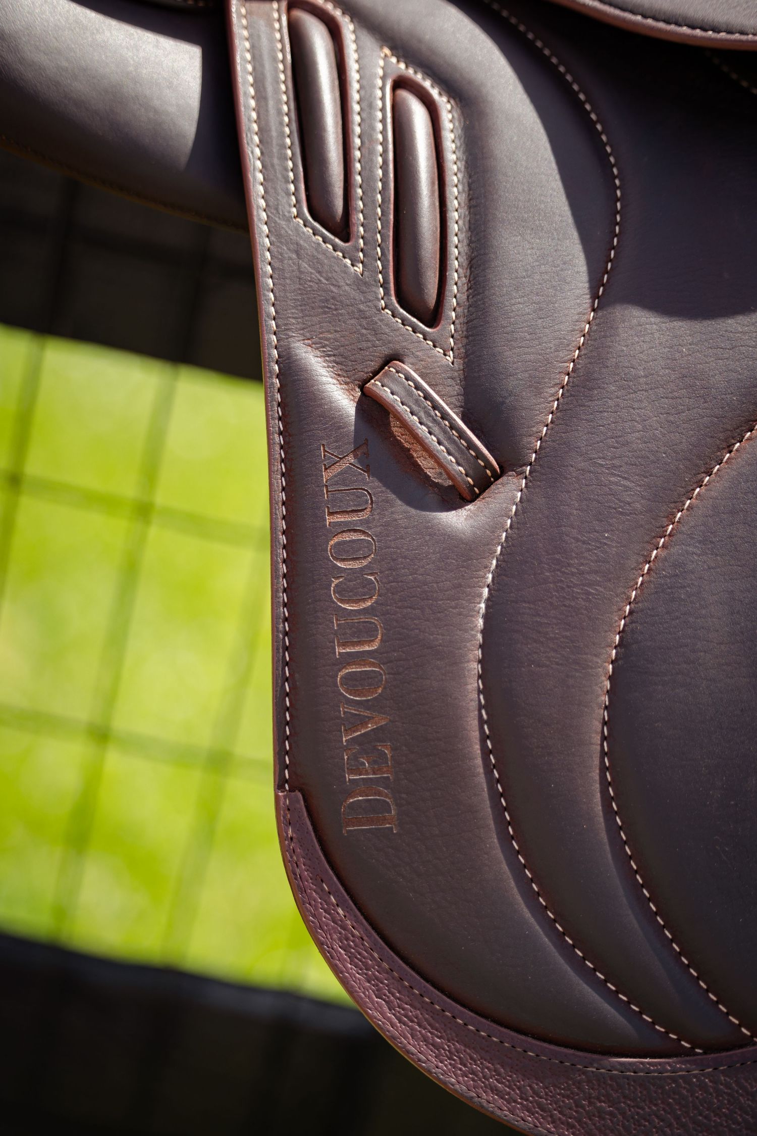 Close-up detail of brown leather dressage saddle with decorative stitching and embossed branding.