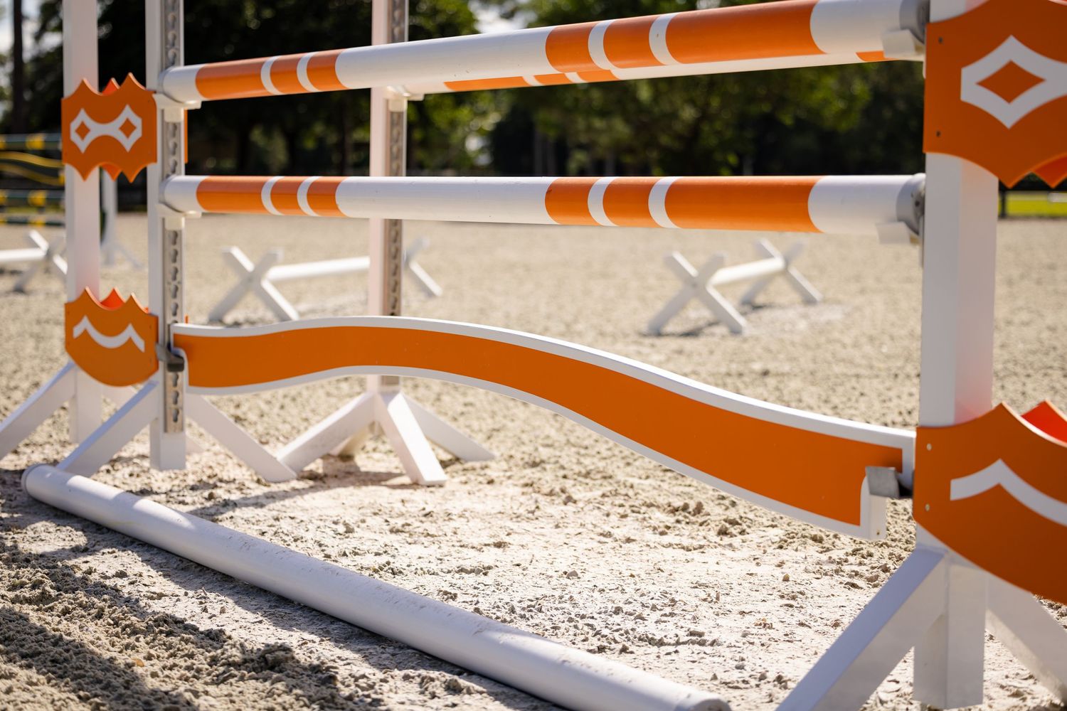 Close-up view of an orange and white striped equestrian jump rail in a sandy arena.