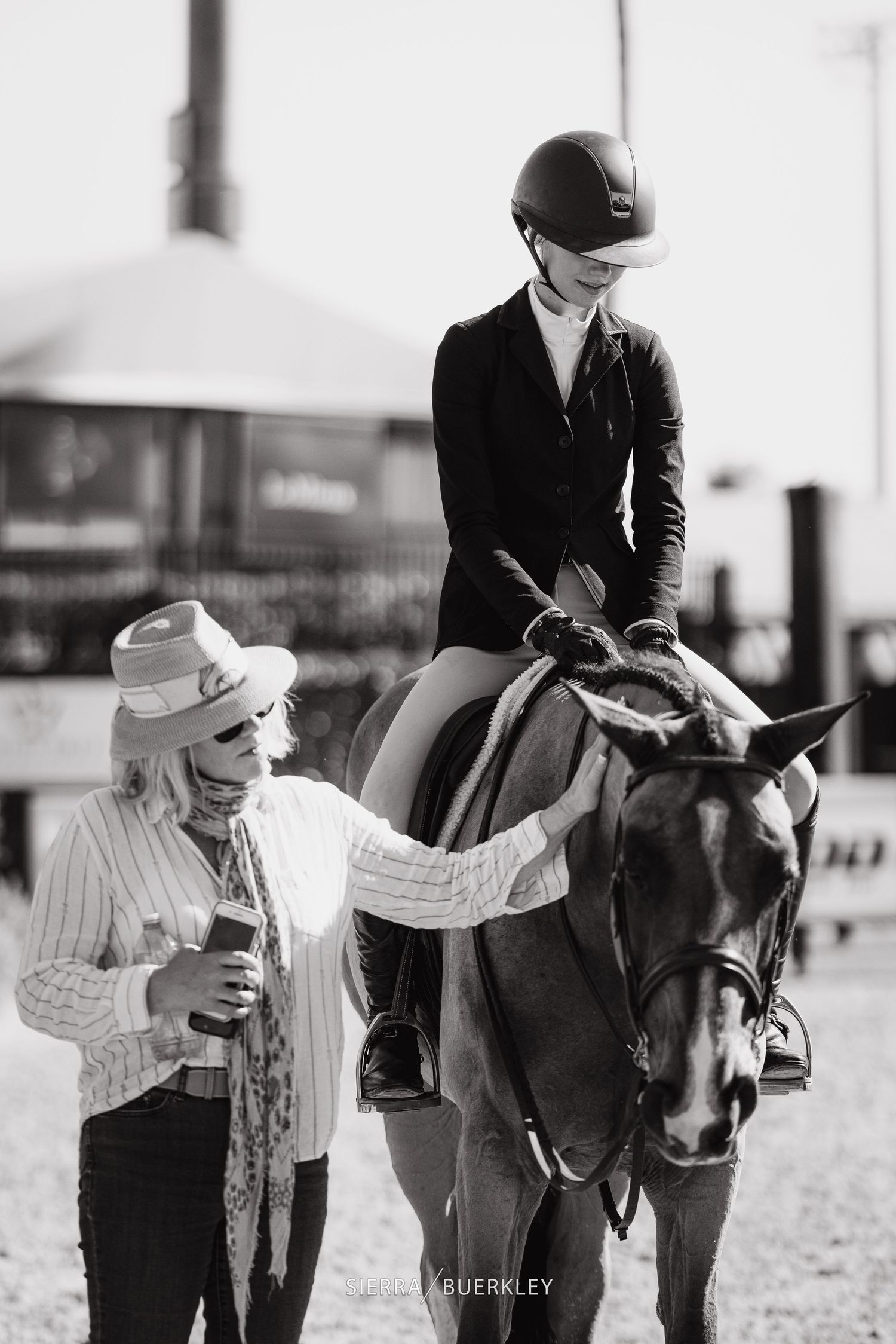 Black and white photo of equestrian training session with horse and riders at an outdoor arena.