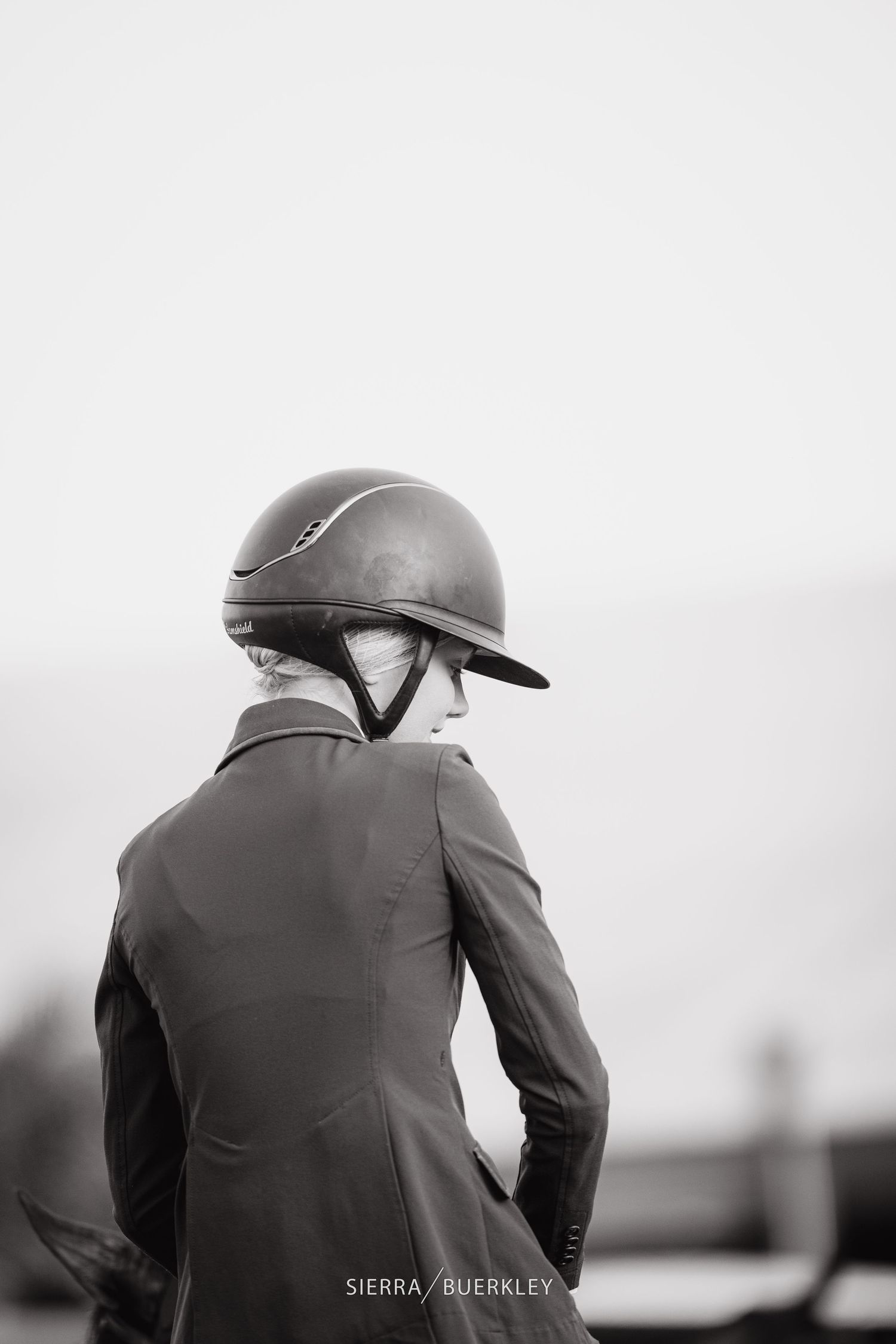 Black and white equestrian portrait showing a rider in formal competition attire and helmet from behind.