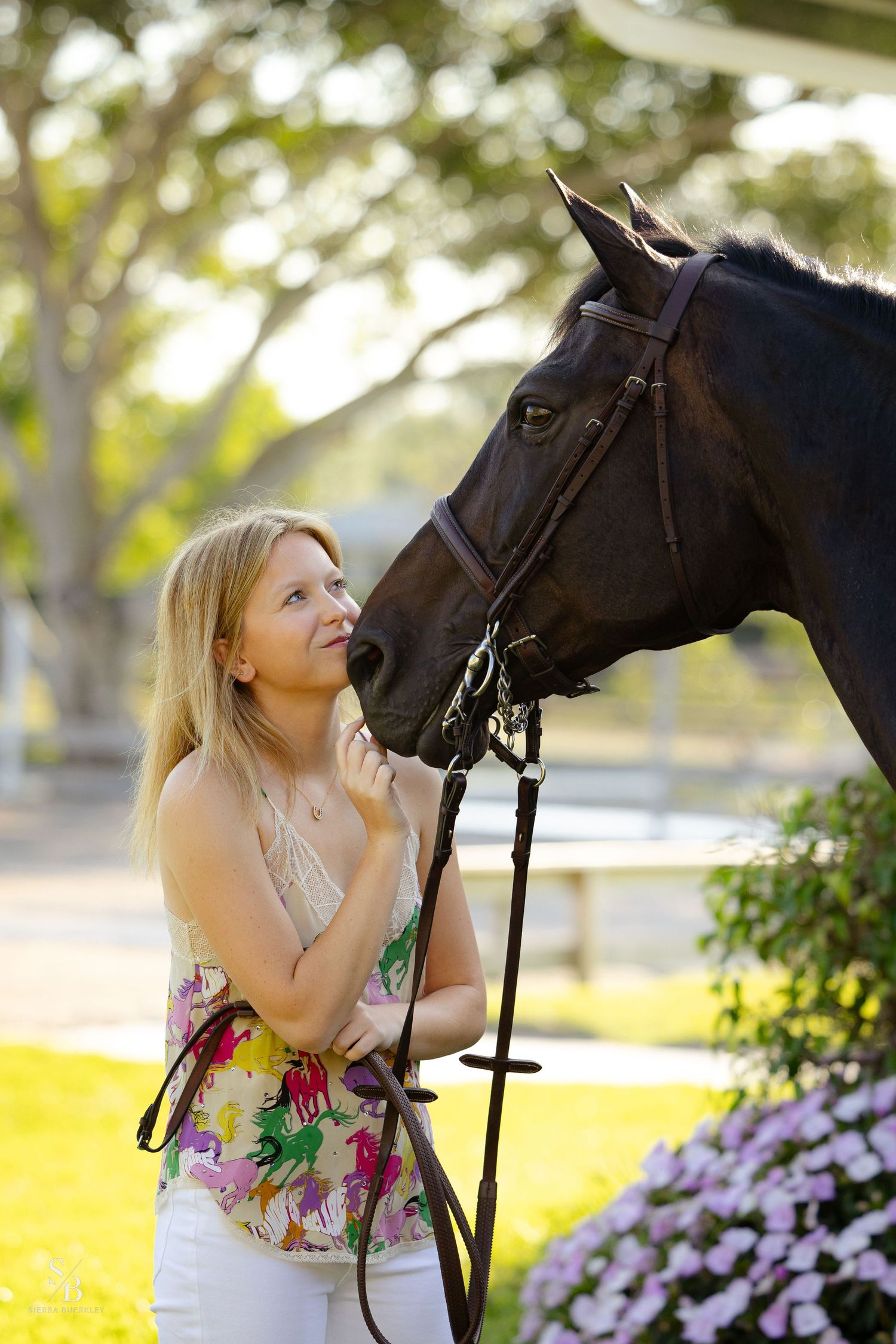 A dark horse and companion share an affectionate moment near blooming flowers.