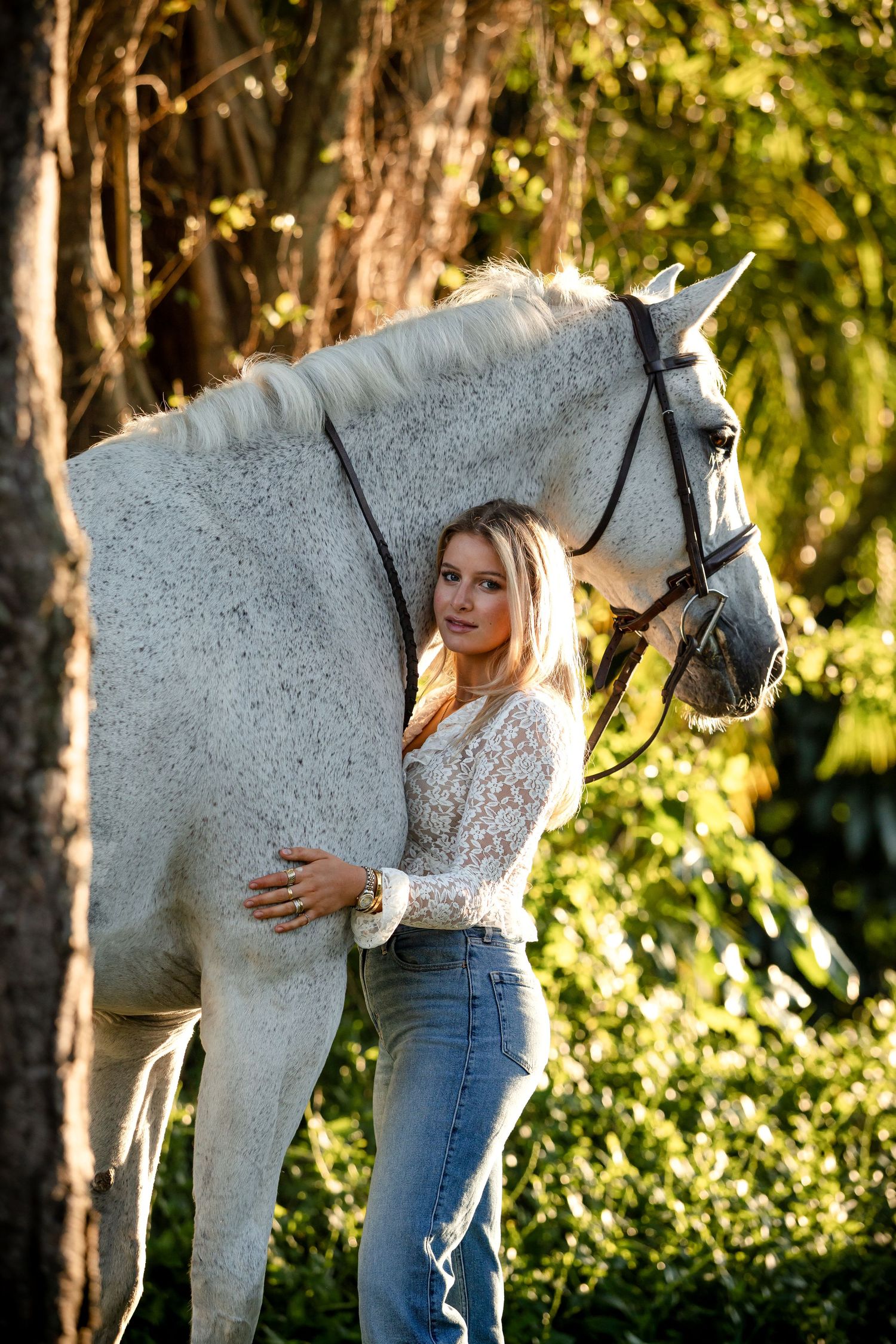 A white horse stands in a sunlit forest while someone in jeans gently embraces its neck in a series of tender moments.