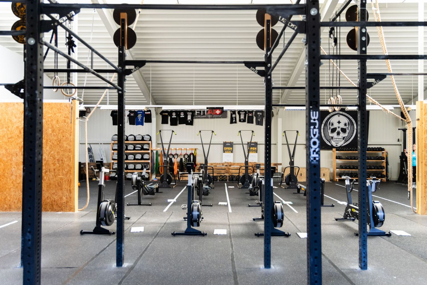 Bild einer Sporthalle einer Crossfitbox mit ganz vielen Sportgeräten, Rudergeräten und Gewichten.