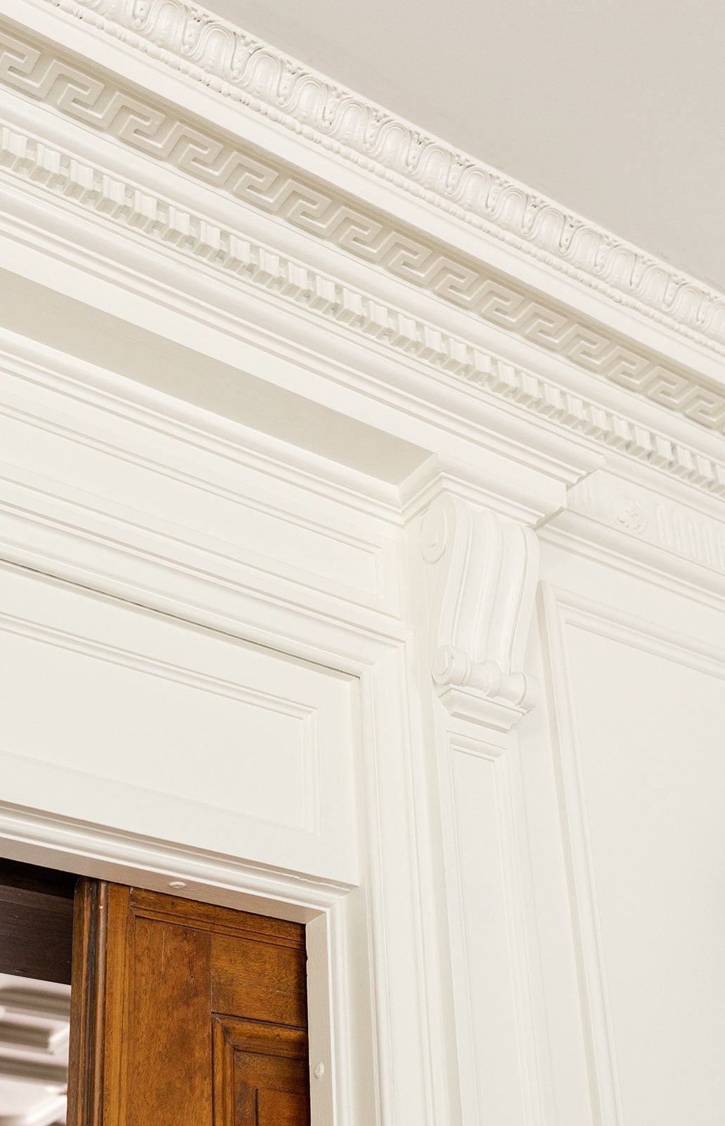 Detailed white crown molding meets dark wooden doorframes in an ornate interior architectural detail.