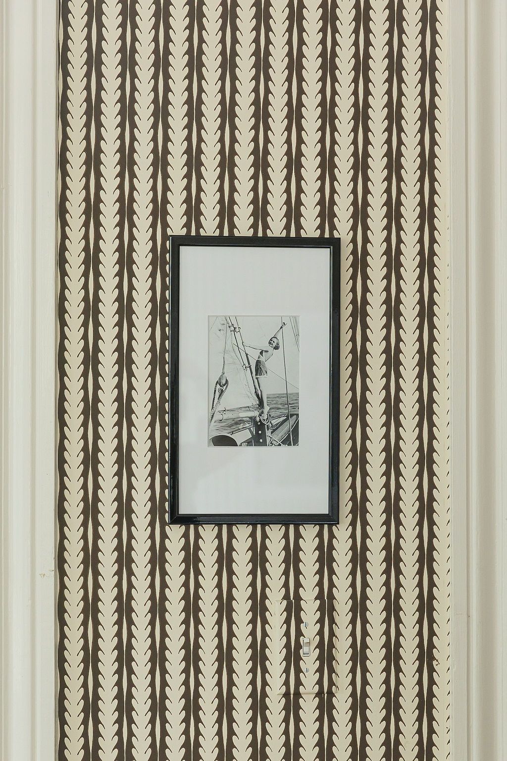 A retro interior wall features geometric patterned wallpaper and three framed black and white artwork prints.
