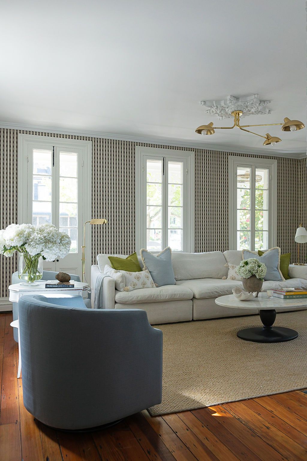Elegant living room with striped wallpaper, cream sofa, blue accent chair, hardwood floors and French windows.