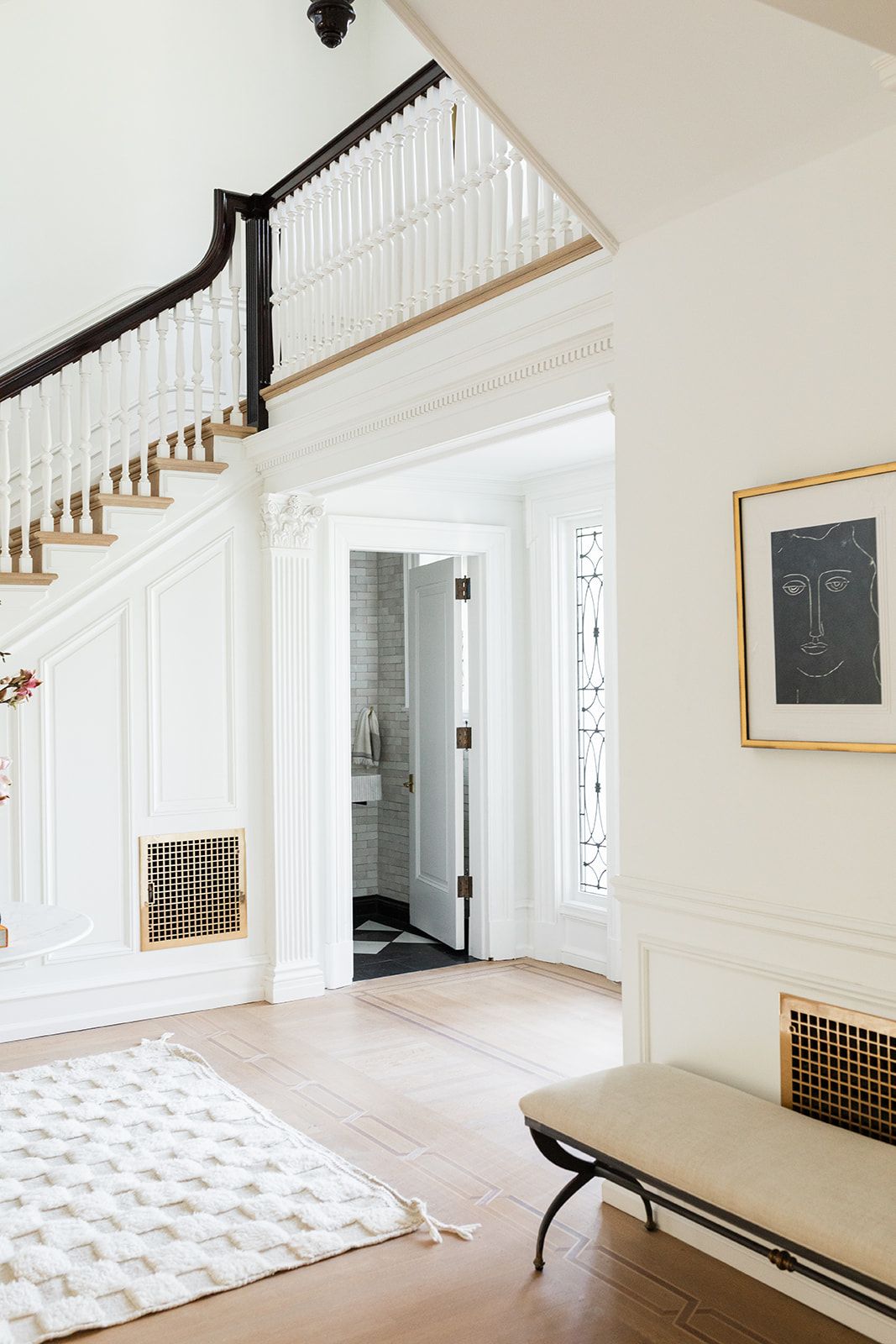 Elegant white foyer with dark wood staircase, wainscoting, and modern bench seating.