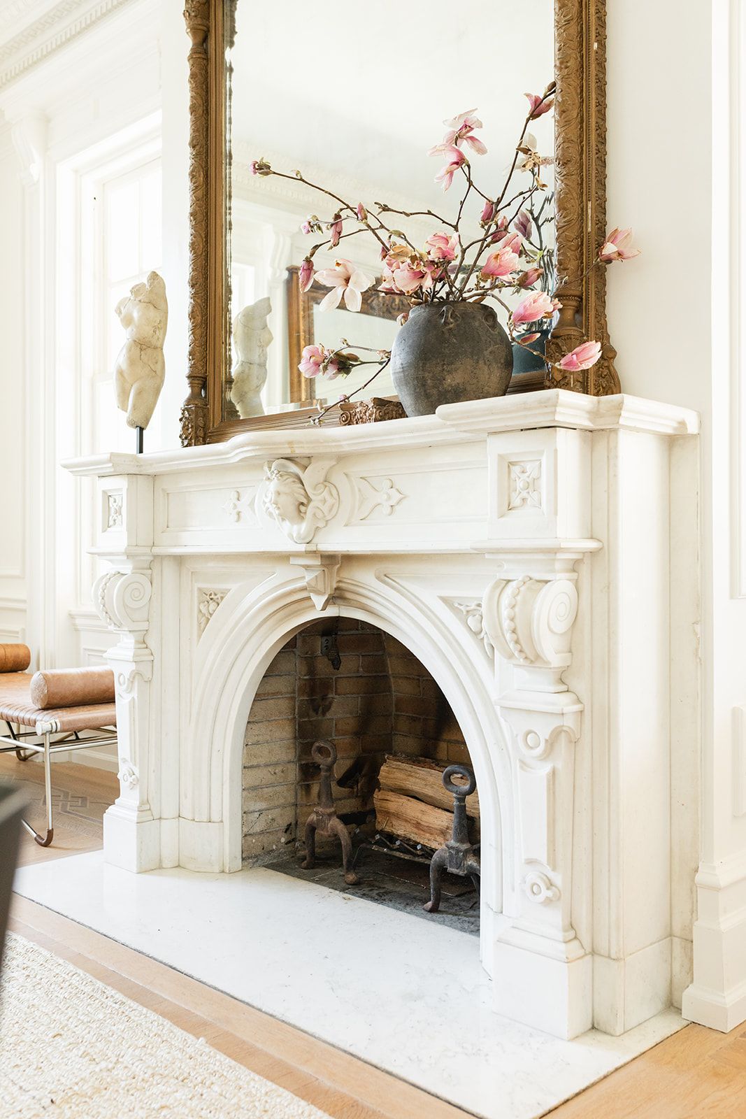 White marble fireplace with ornate carvings and pink floral arrangement in gray vase.