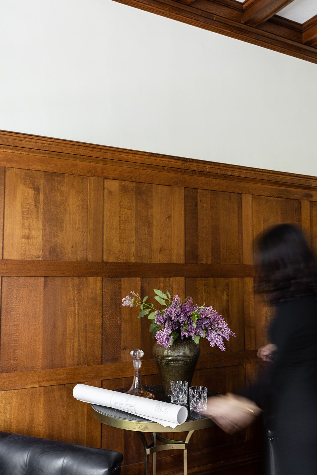 Wood-paneled room with lilac flowers in vase and movement blur against warm wooden walls.