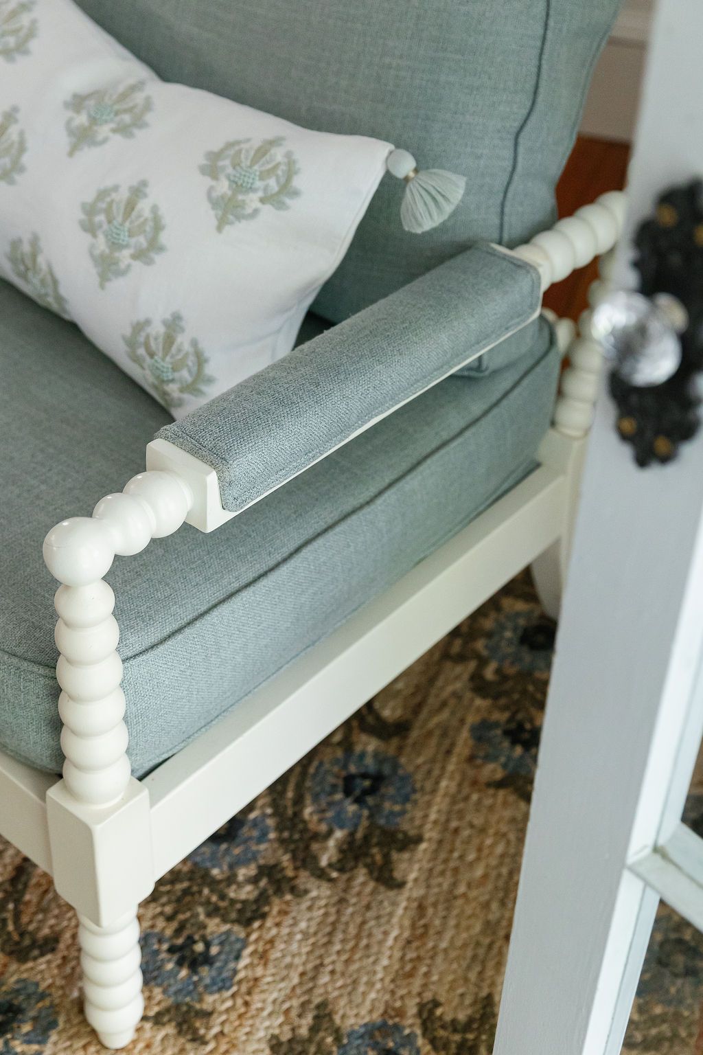 Close-up view of a white spindle chair armrest with gray cushioning against a floral wallpaper background.