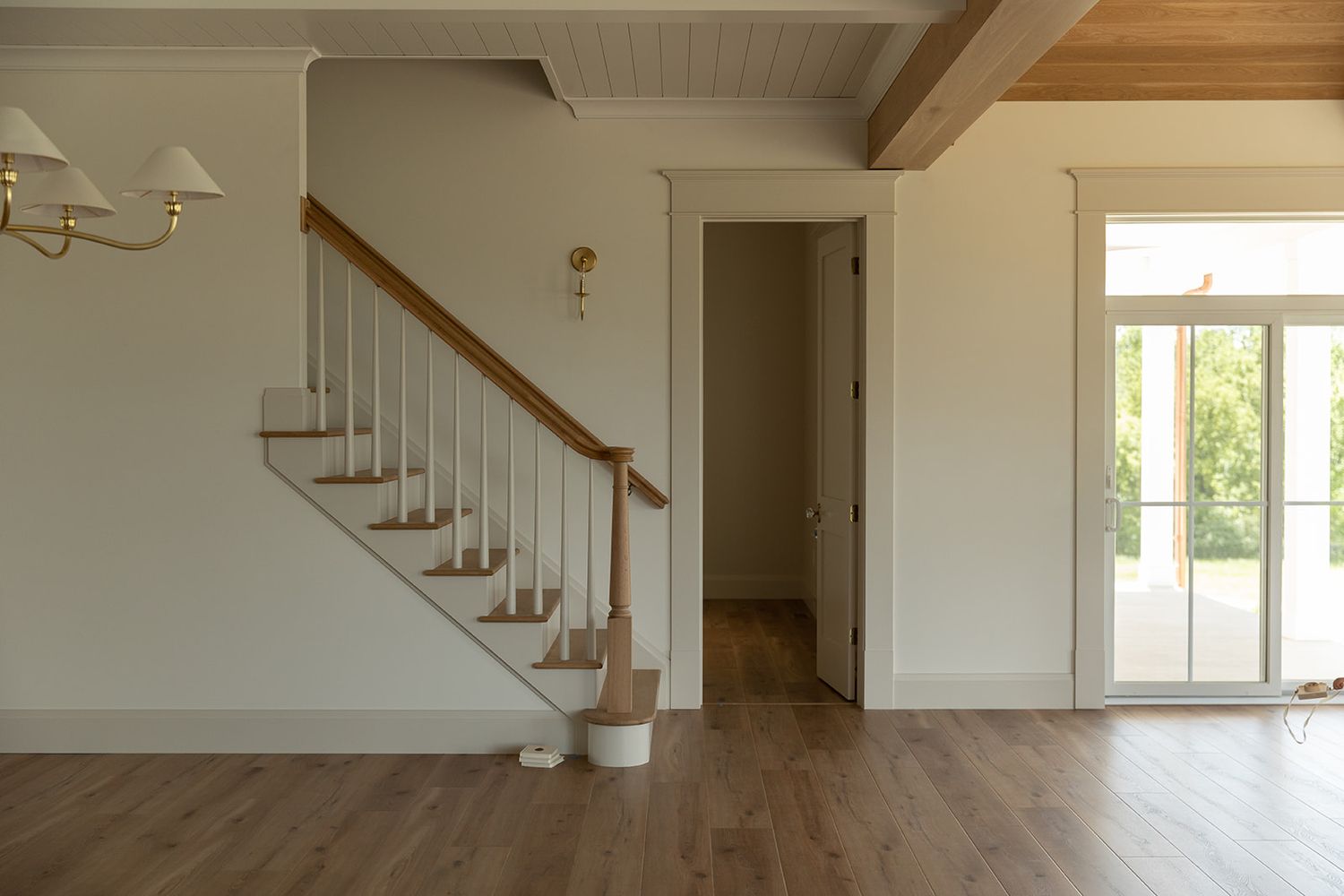 Bright open-concept home interior featuring white staircase, wood railings, hardwood floors, and large glass door with natural light.