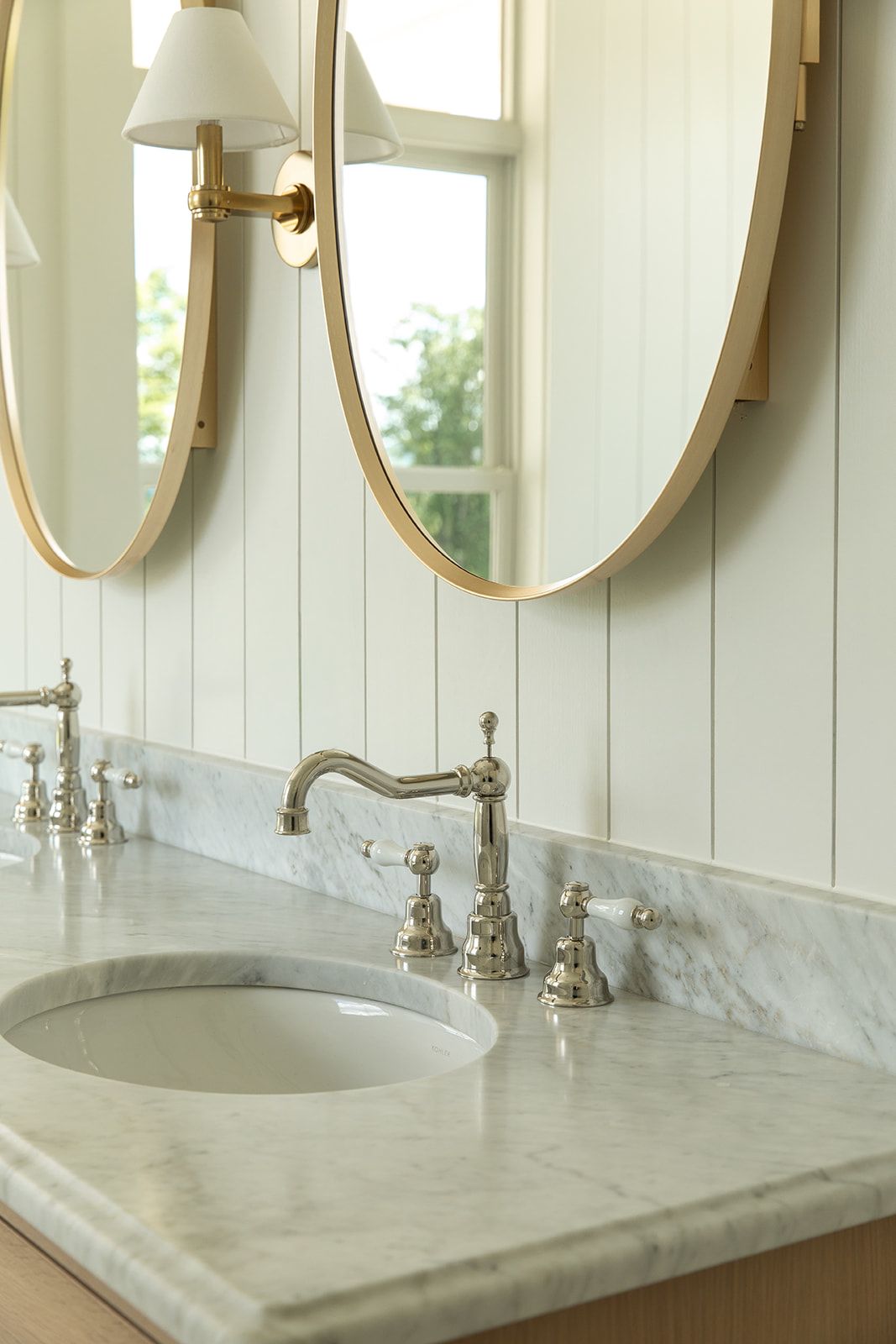 Elegant marble bathroom vanity with polished nickel faucet, undermount sink, and gold-framed oval mirrors on white shiplap wall.