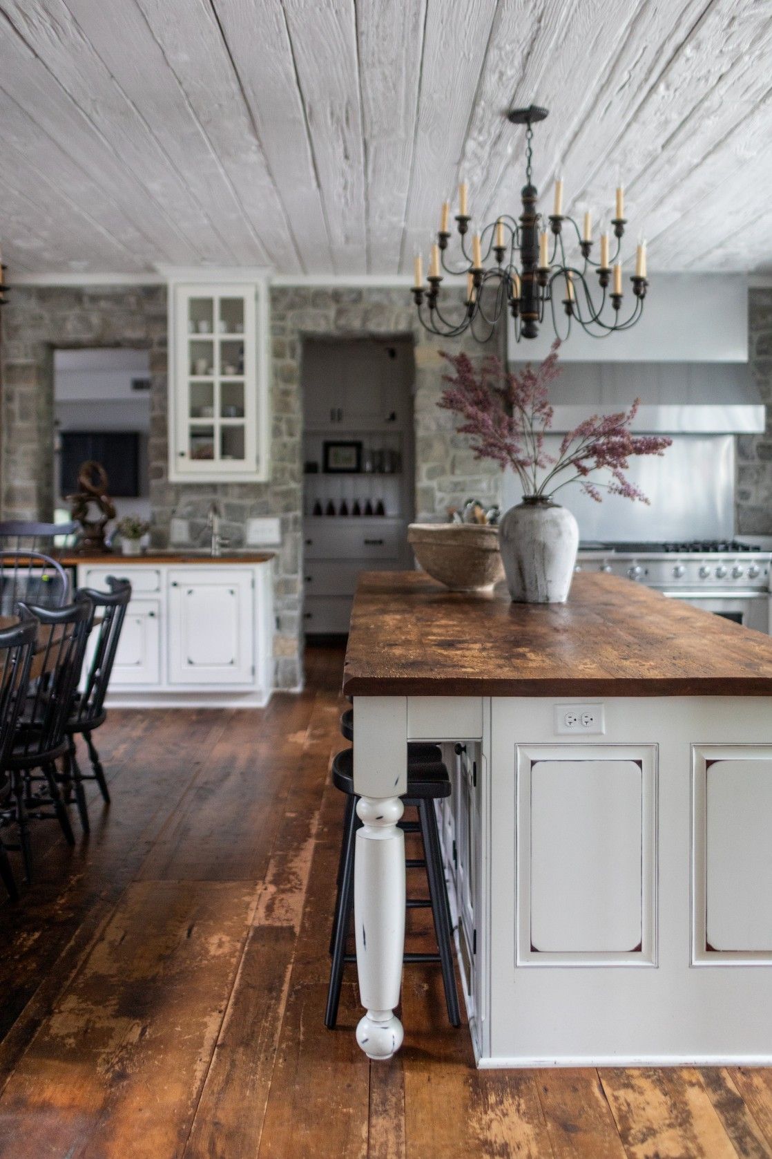 Rustic farmhouse kitchen with white cabinets, butcher block island, chandelier, and wide plank hardwood flooring.