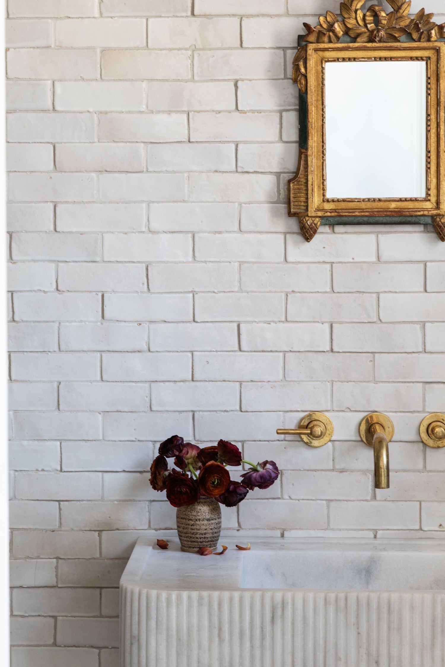 White bathroom sink with vintage gold mirror and brass fixtures mounted on white brick wall.